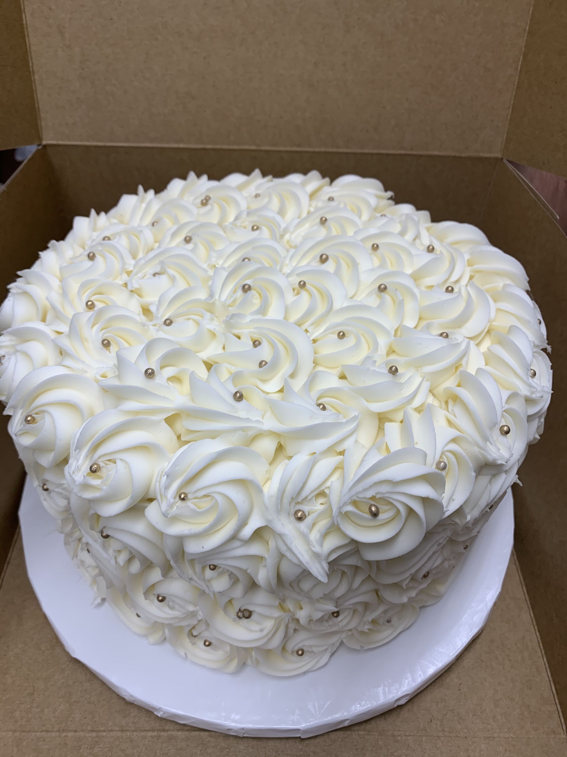 a white cake with white frosting and gold sprinkles is in a box .