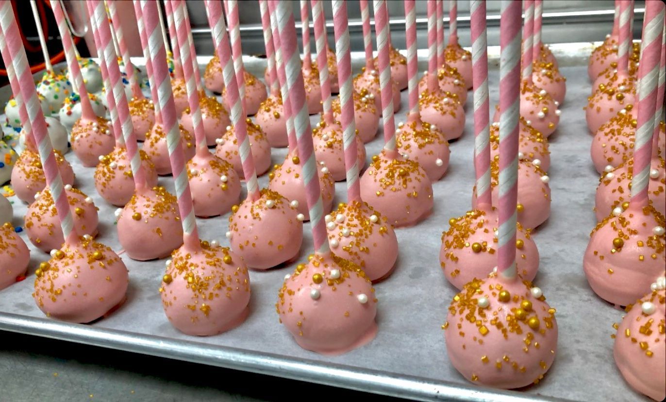 a tray of pink cake pops with gold sprinkles