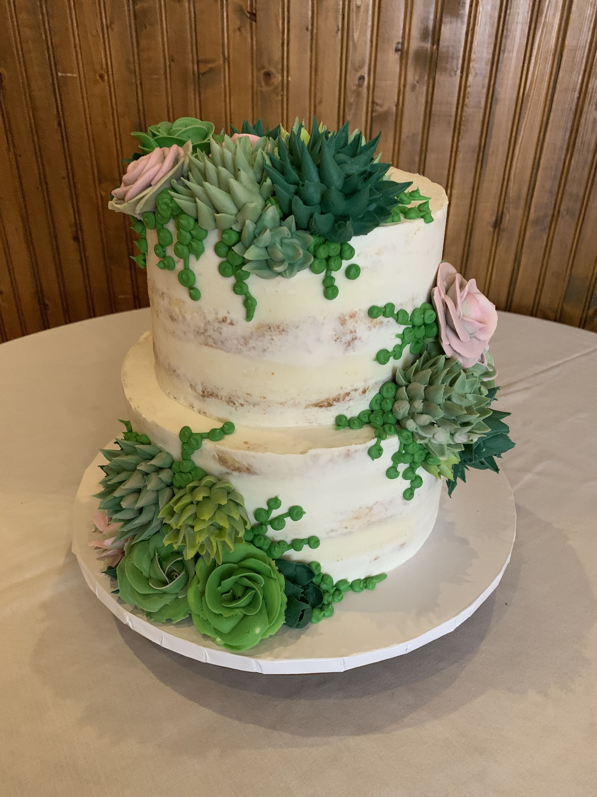 a wedding cake decorated with succulents and flowers is sitting on a white plate on a table .