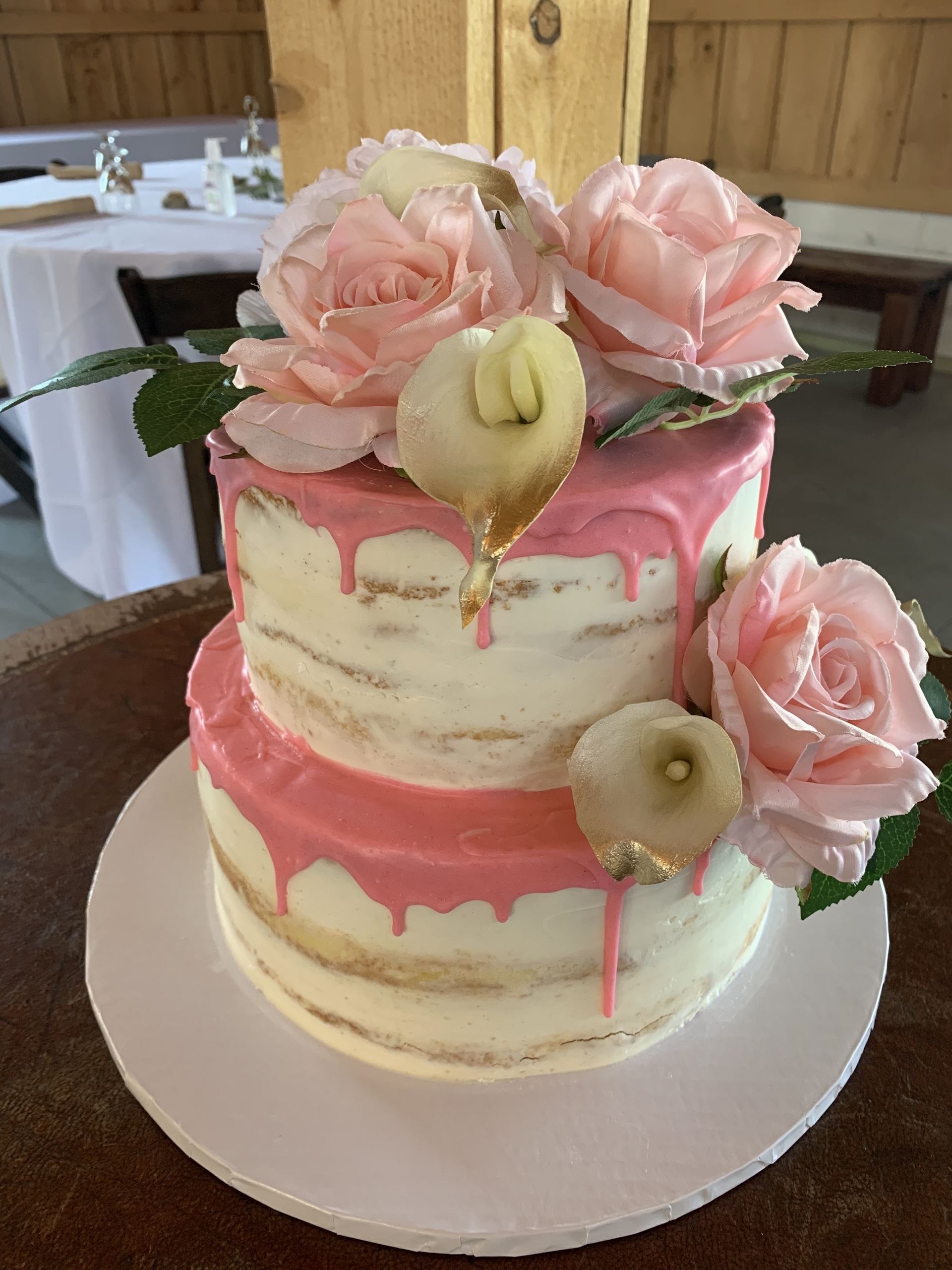 a wedding cake with pink frosting and pink roses is sitting on a table .