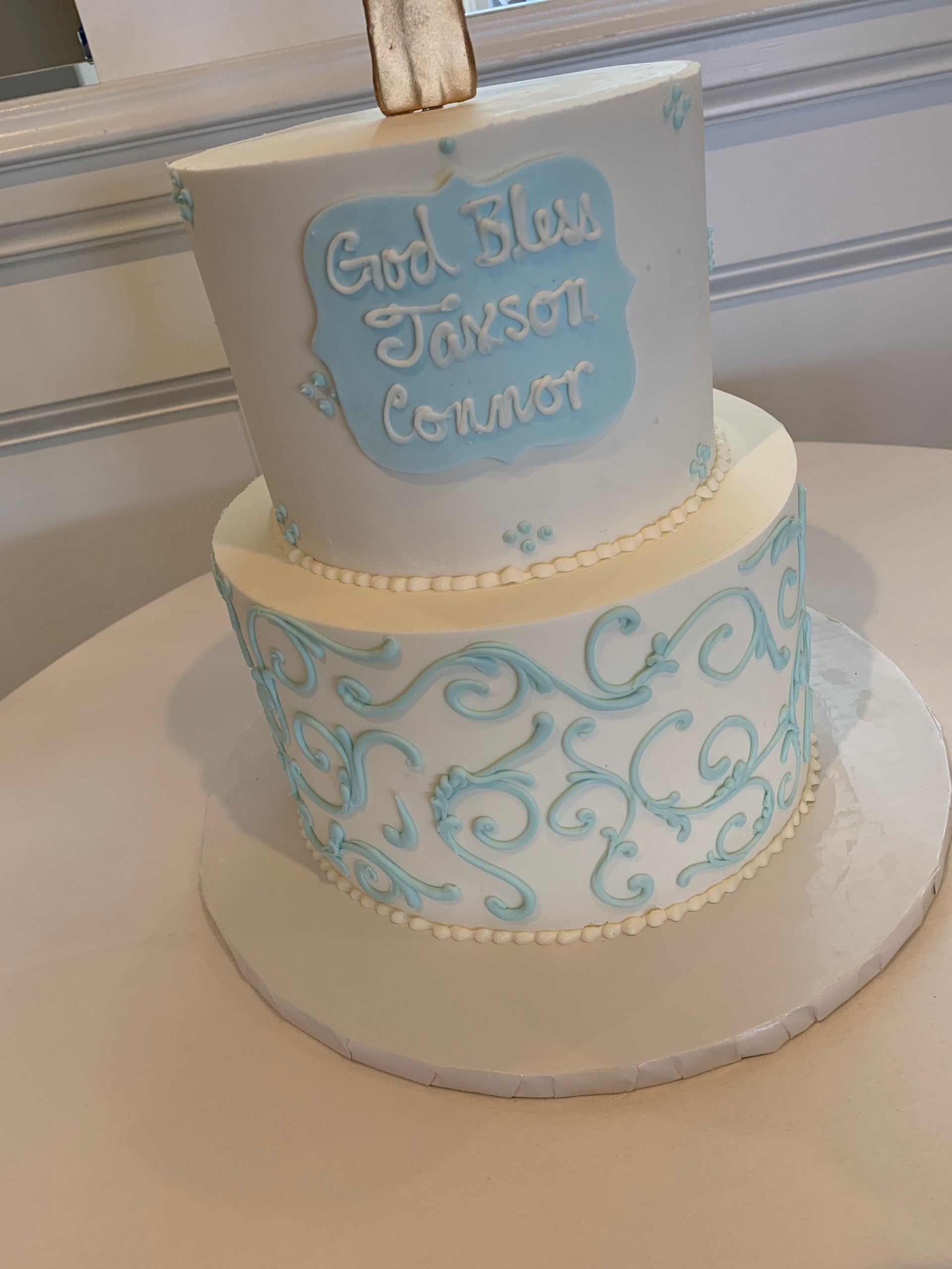 a white and blue cake with a cross on top is sitting on a table .