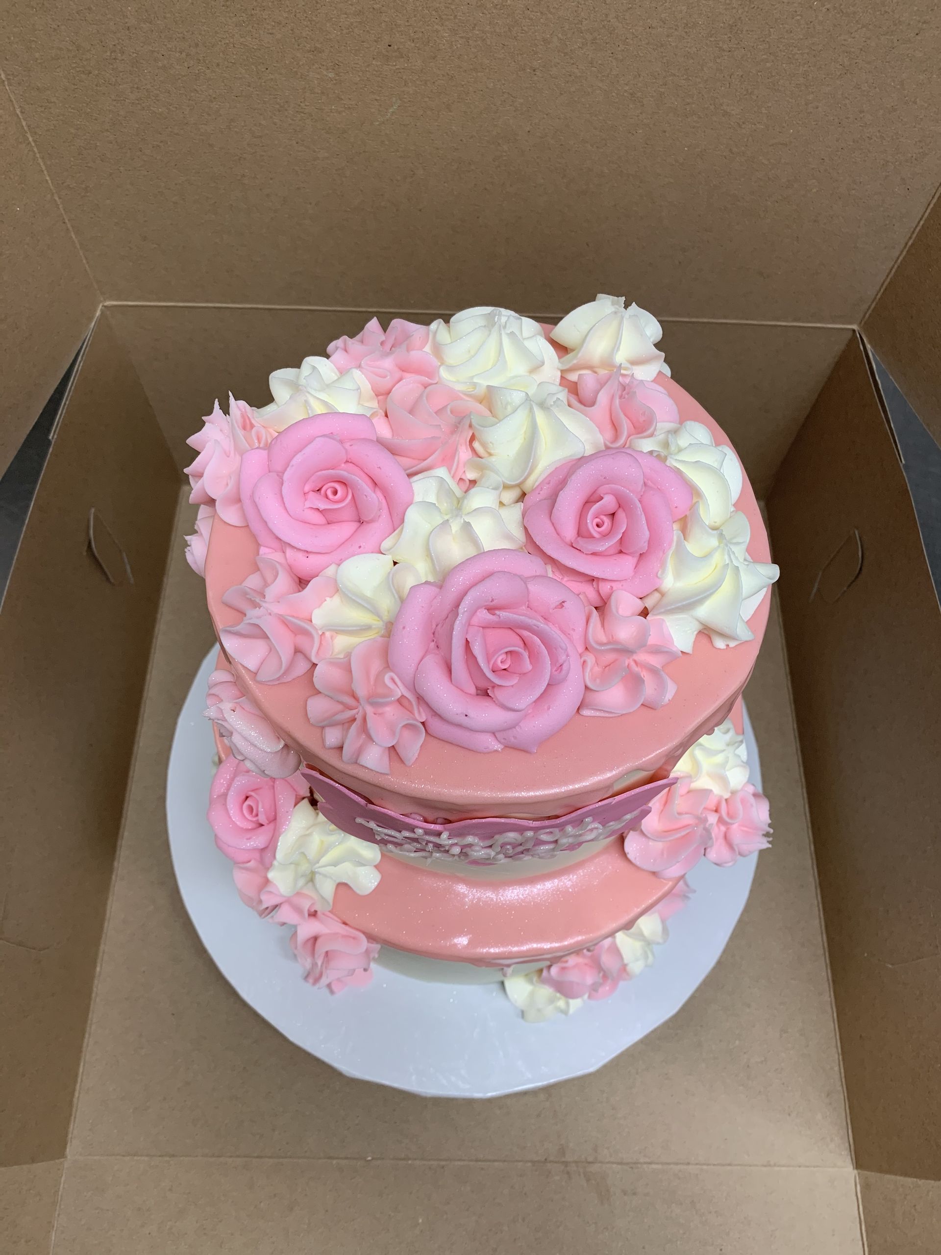 a pink cake with pink roses and white frosting is in a box .