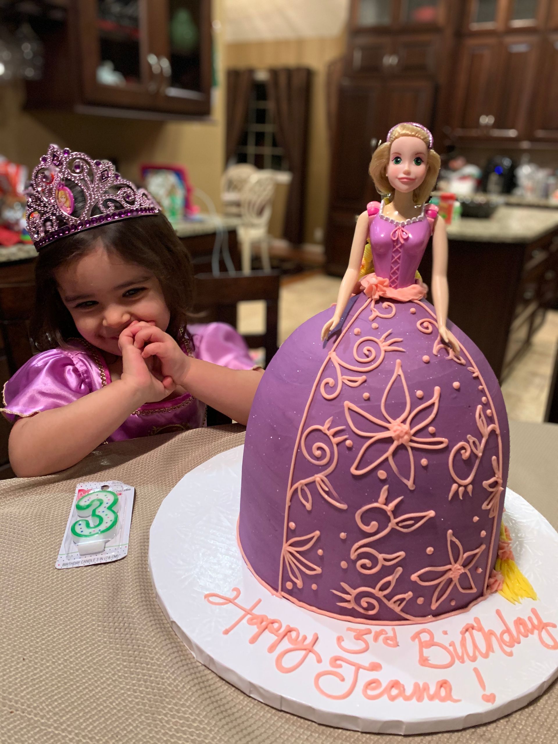 a little girl is sitting at a table with a birthday cake in the shape of a barbie doll .
