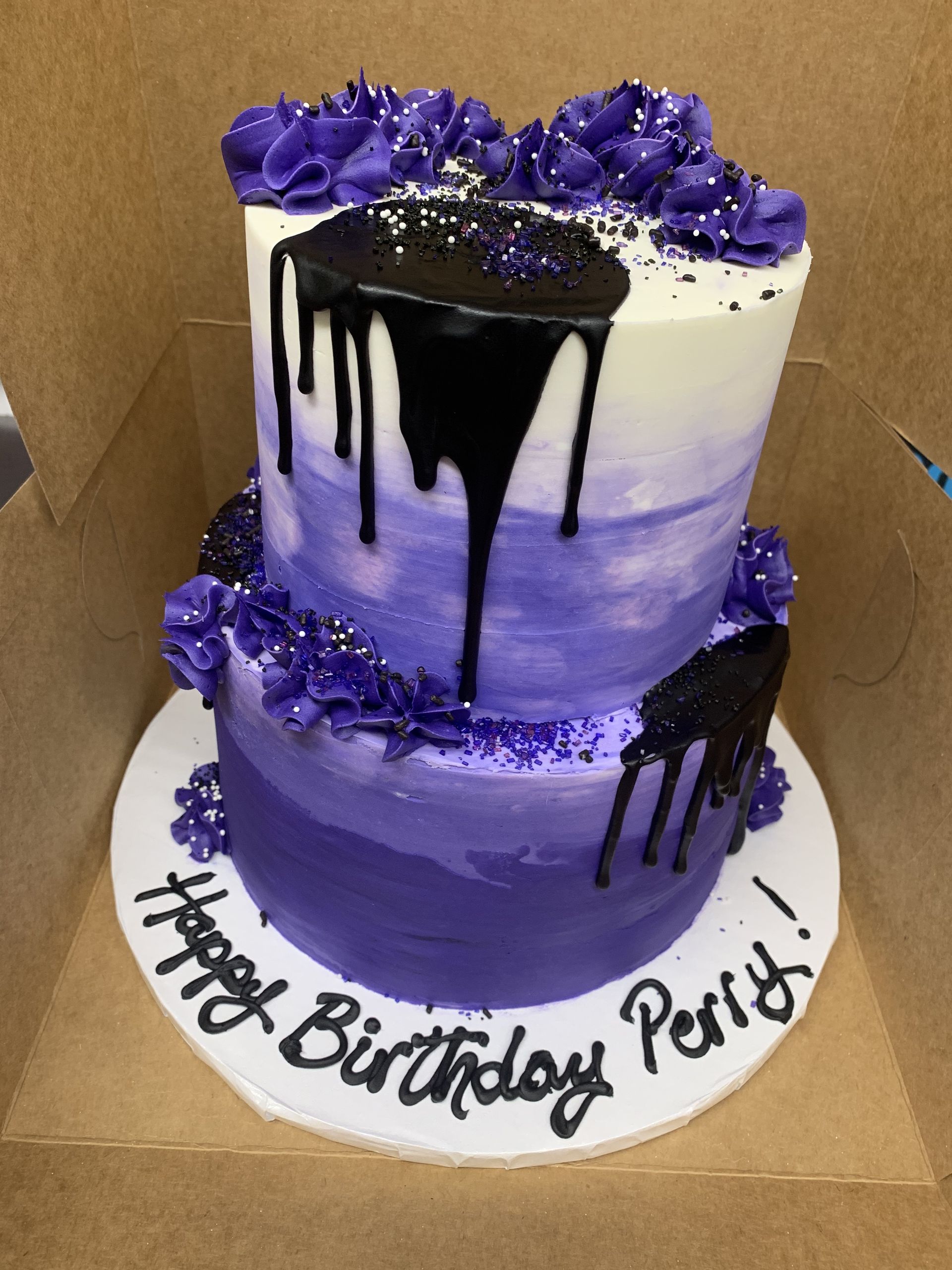 a purple and black birthday cake is in a box