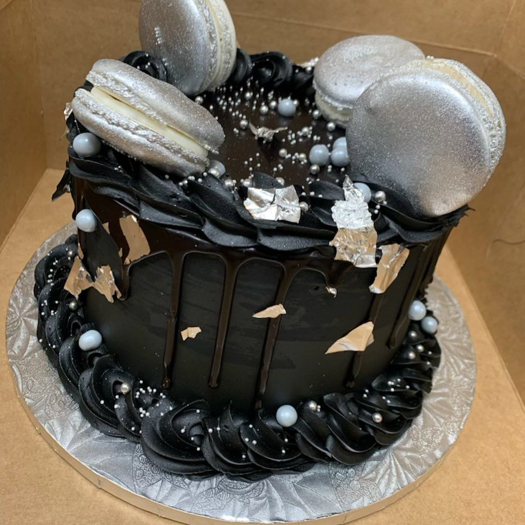 a black cake with silver macarons on top is in a box .