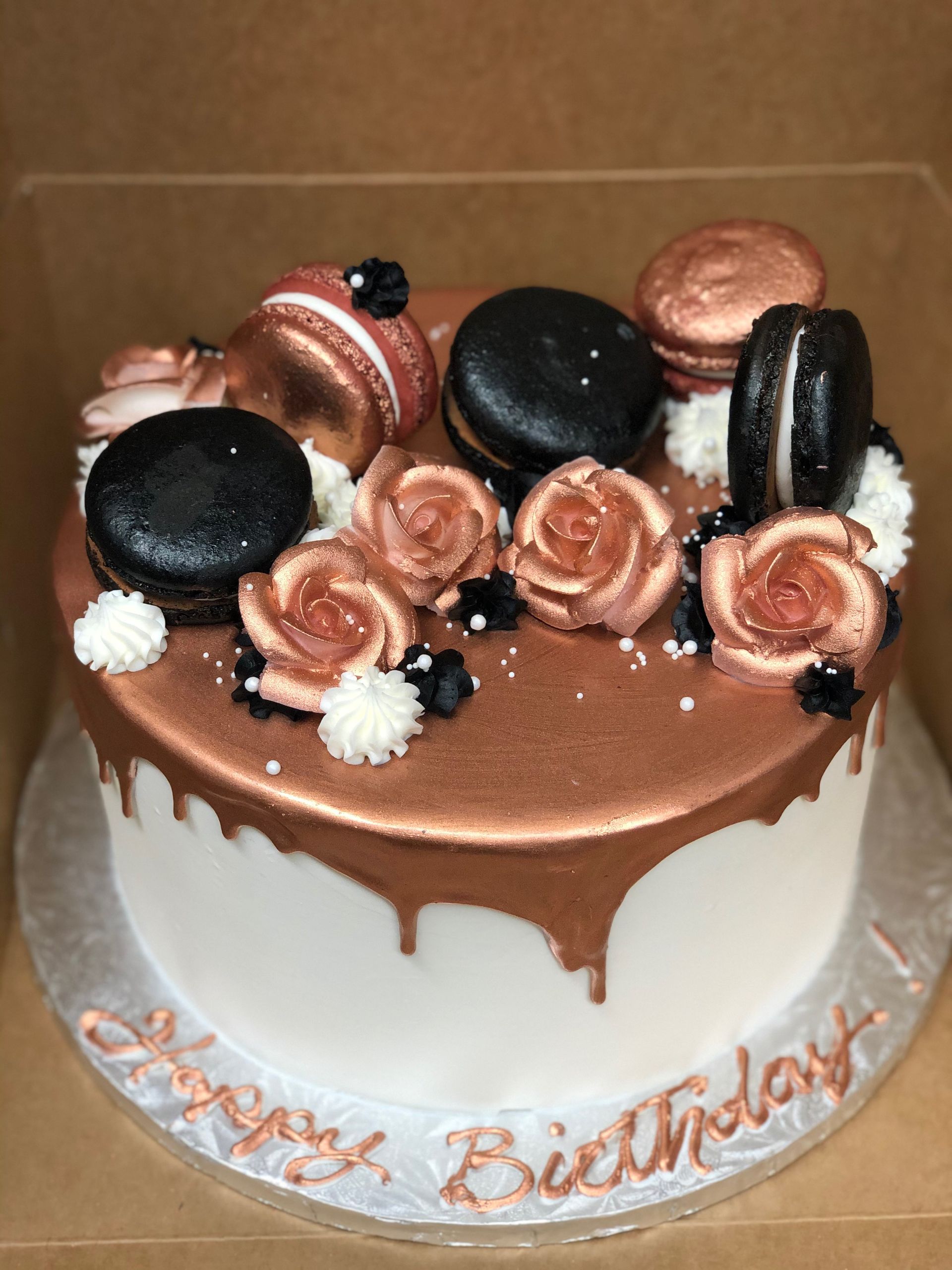 a birthday cake with roses and macarons on it is in a box .