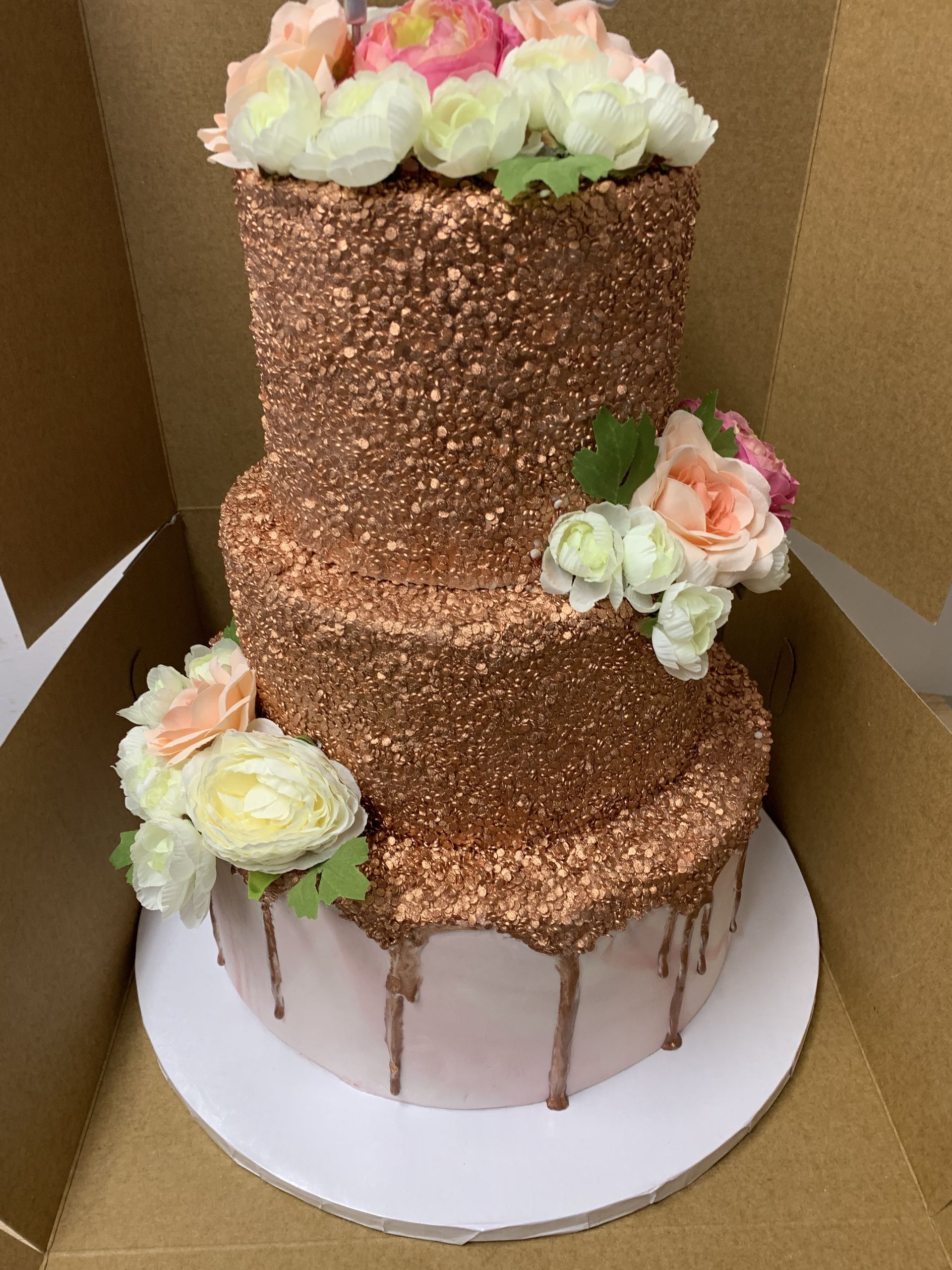 a three tiered cake with flowers on top is in a cardboard box .