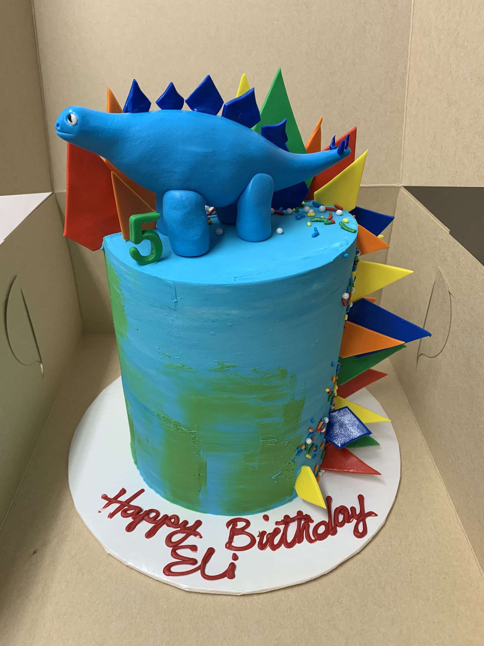 a blue and green birthday cake with a dinosaur on top