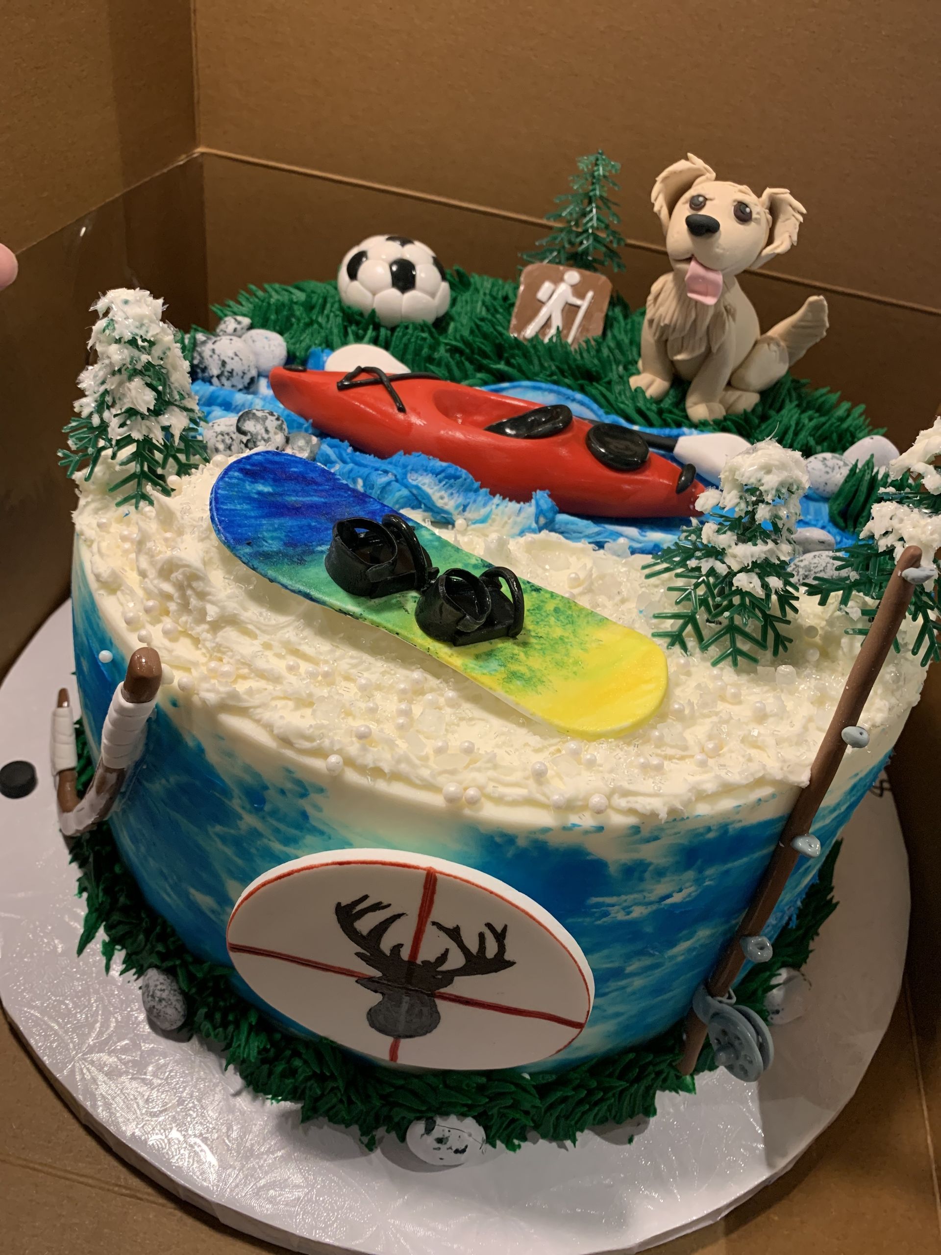 a cake with a dog , kayak , snowboard , and fishing rod on it .