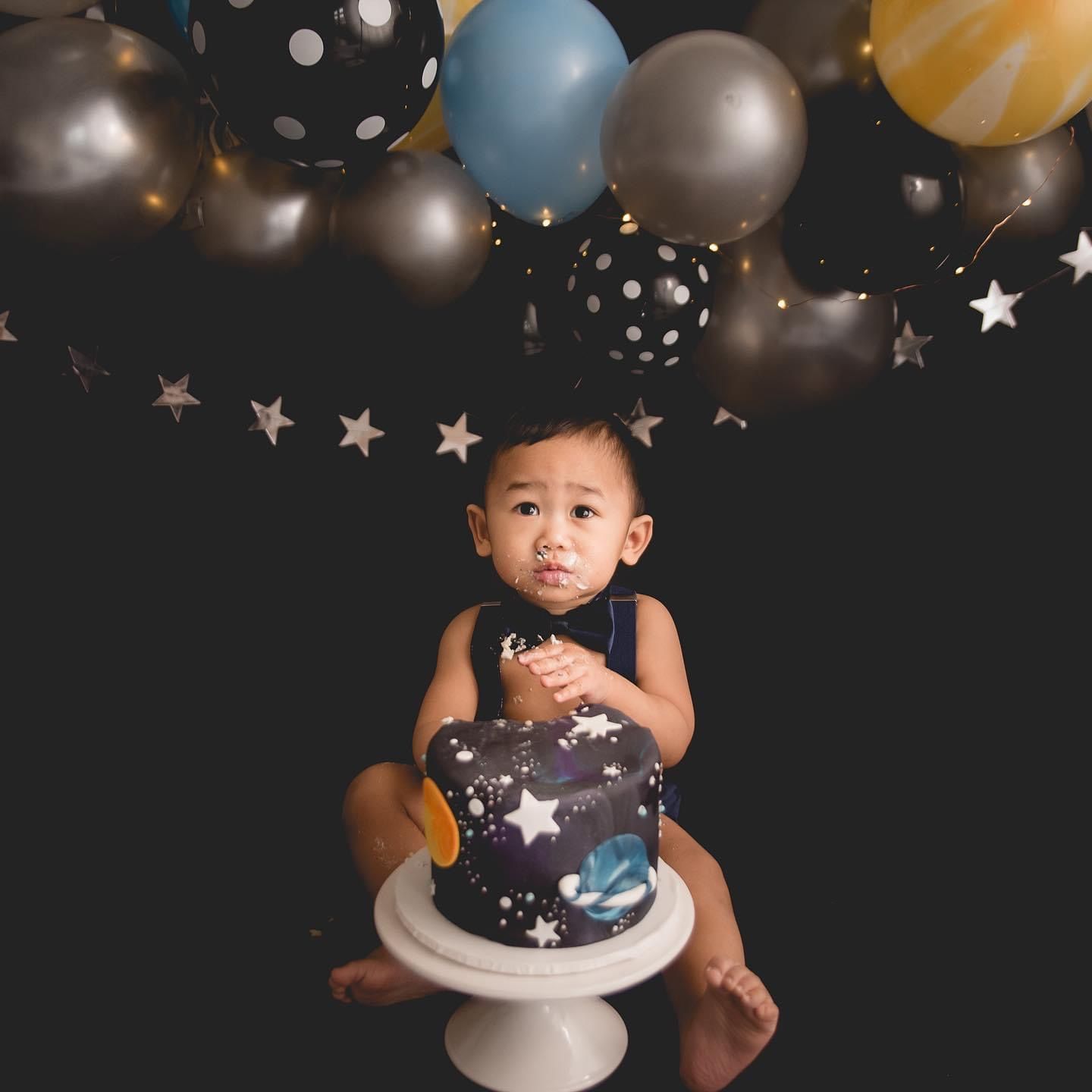 a baby is sitting on a cake in front of balloons .