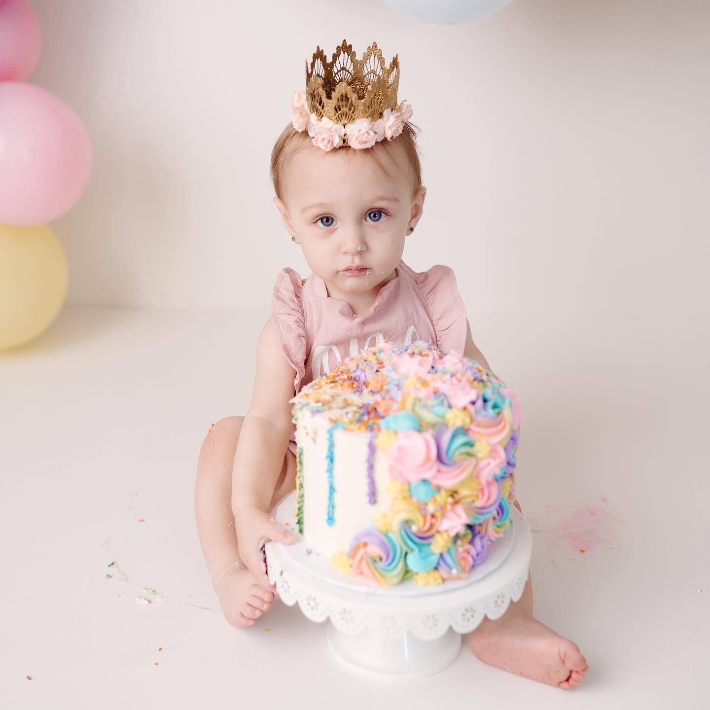 a baby girl wearing a crown is sitting next to a cake .