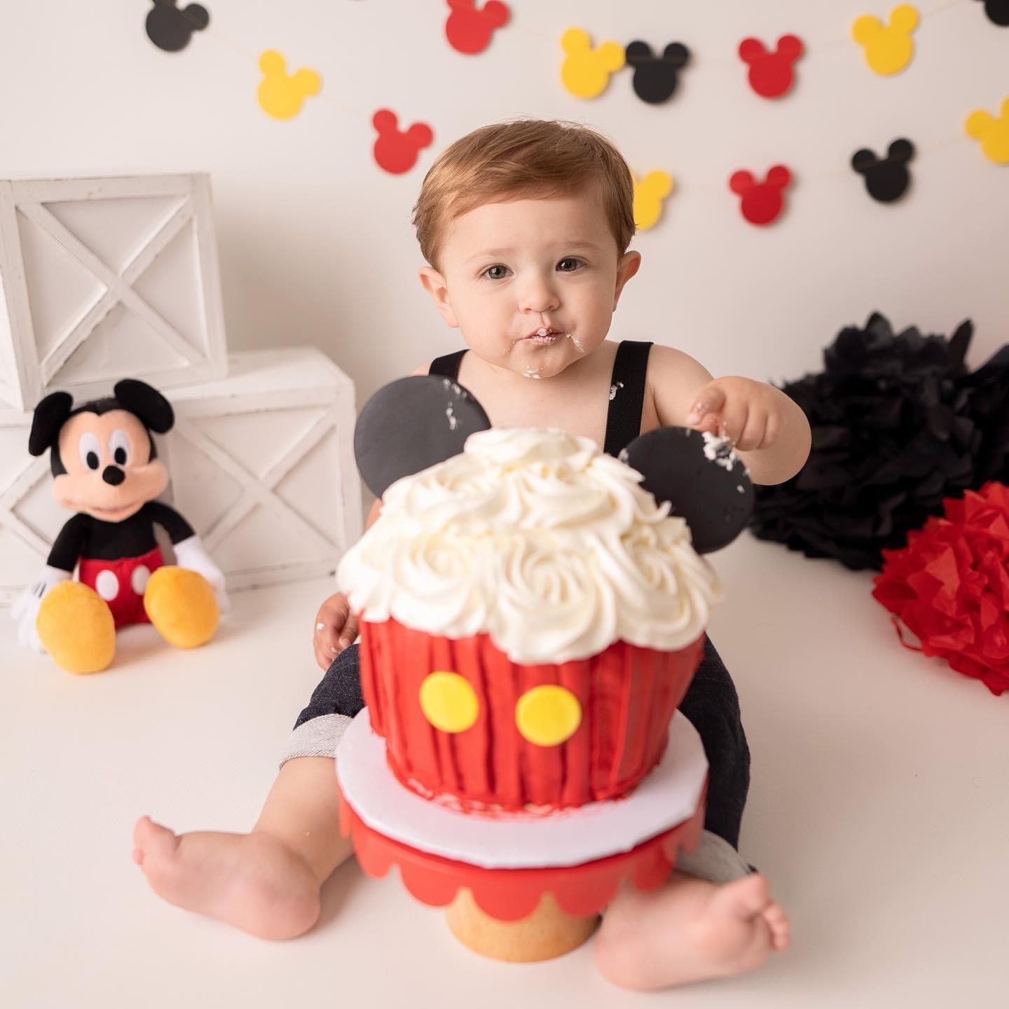 a baby is sitting next to a giant mickey mouse cupcake