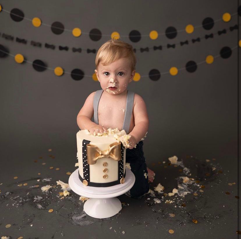 a baby is standing next to a cake on a cake stand .