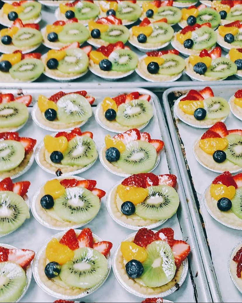 a tray of fruit tarts with kiwi strawberries and blueberries