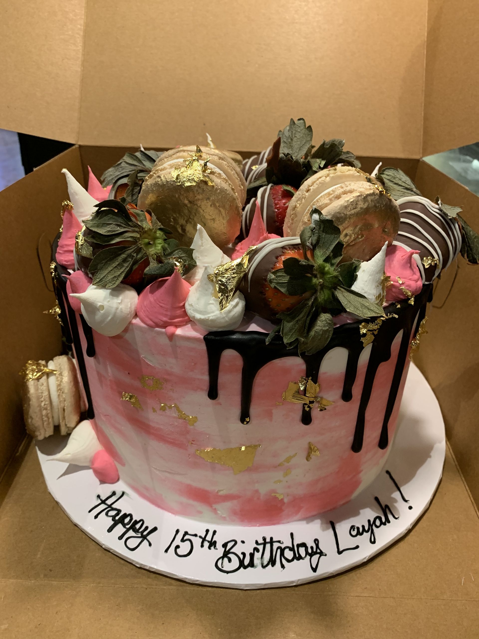 a pink and white birthday cake with strawberries and macarons