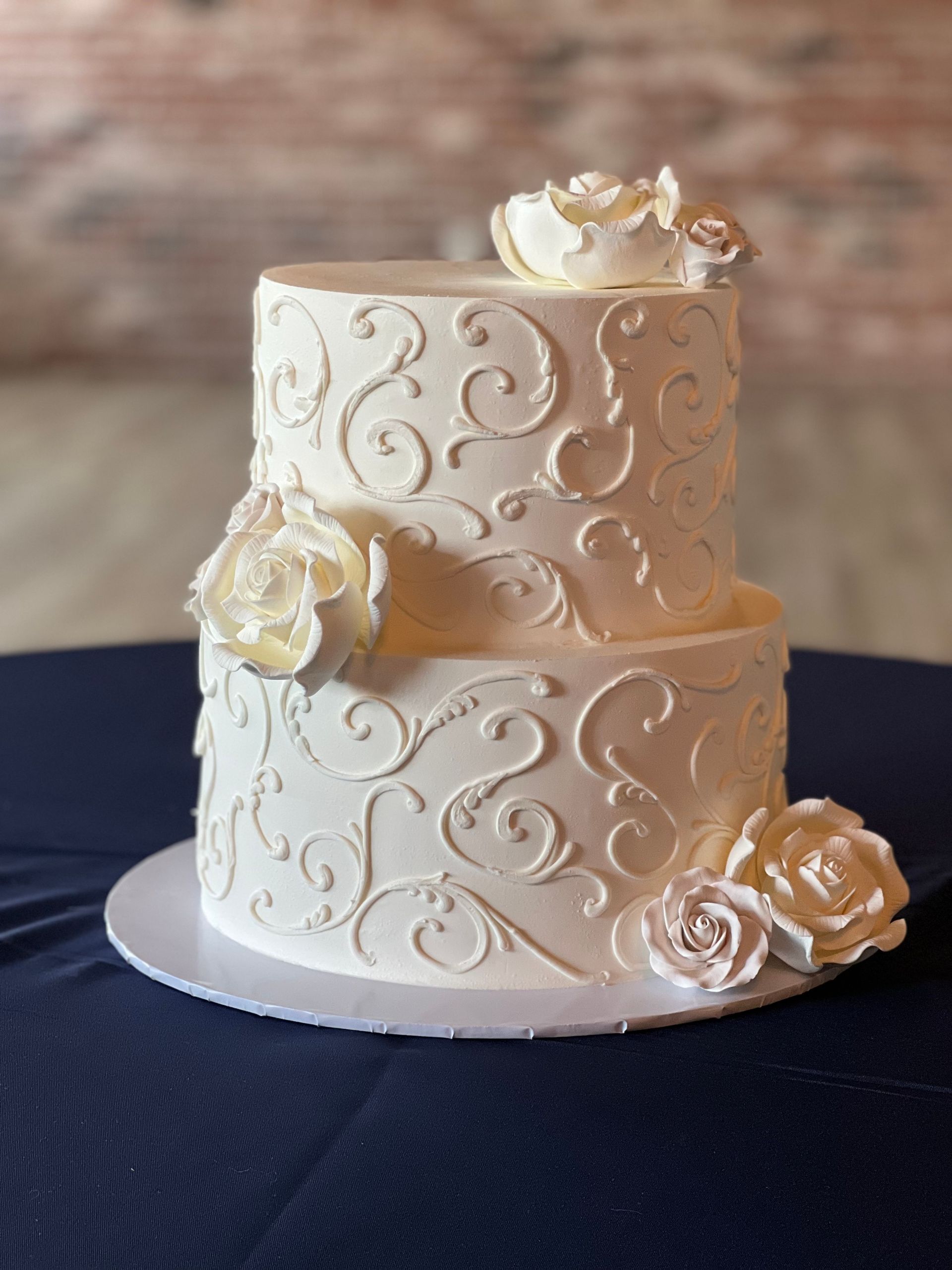 a white wedding cake with white roses and swirls is sitting on a table .
