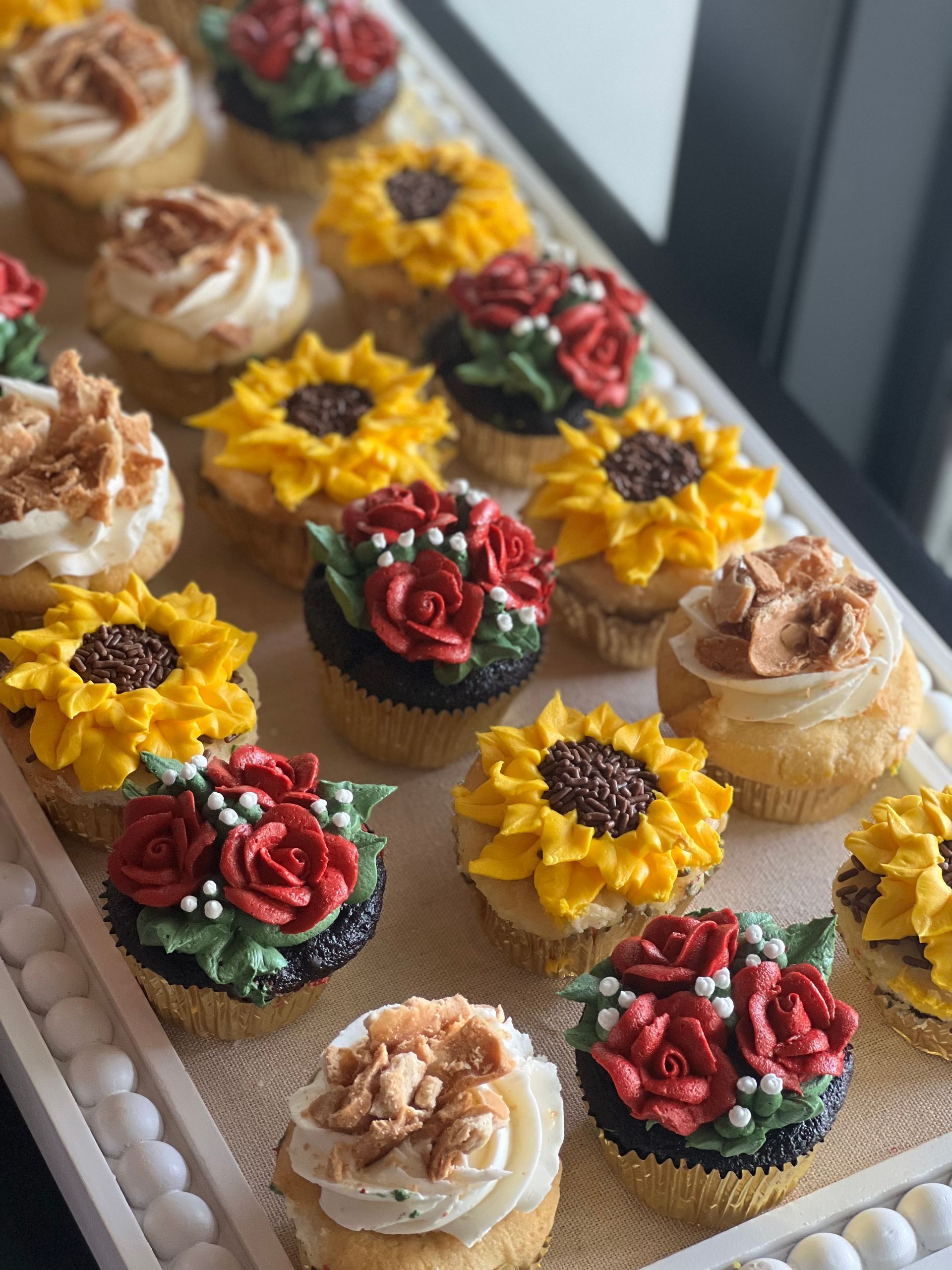 a tray of cupcakes decorated with sunflowers and roses
