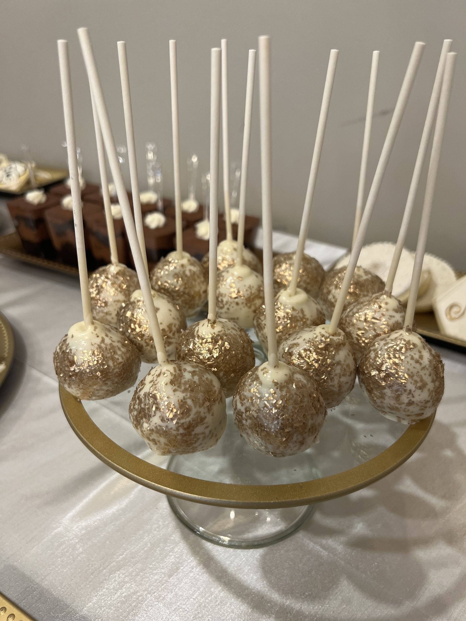 a glass bowl filled with gold cake pops on sticks on a table .