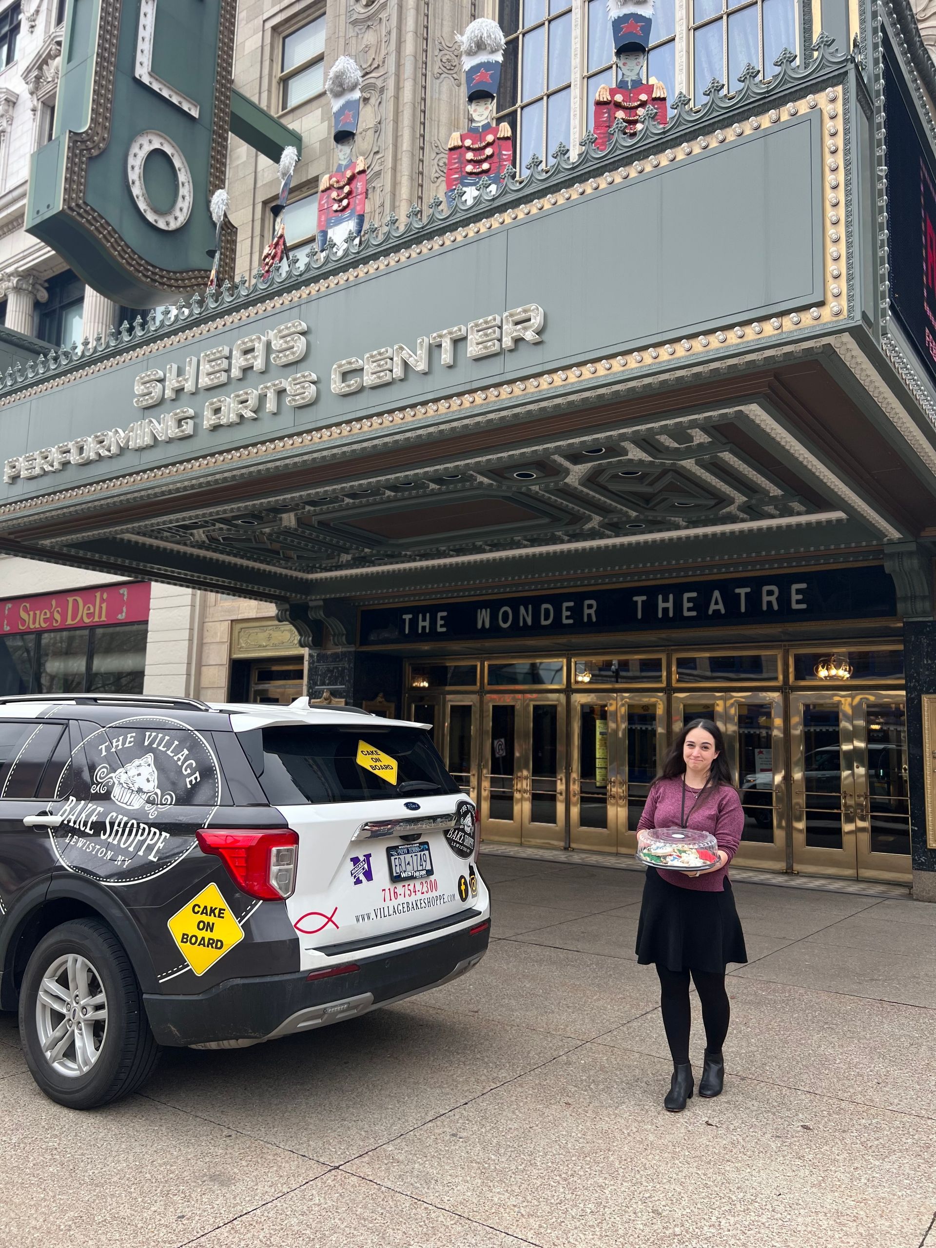 a woman is standing in front of a theater with a car parked in front of it .