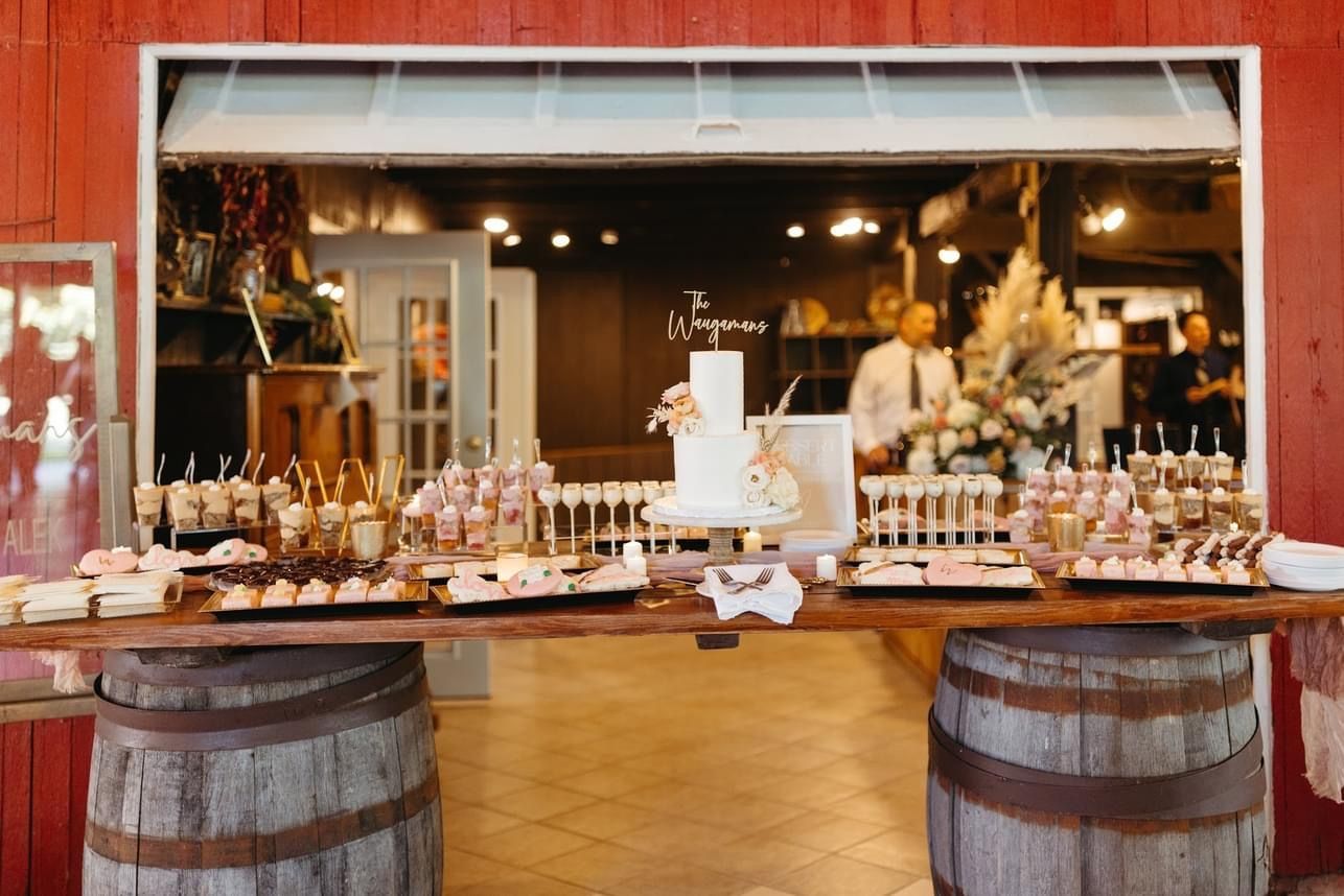 a table with a cake and desserts on it in front of a red barn .