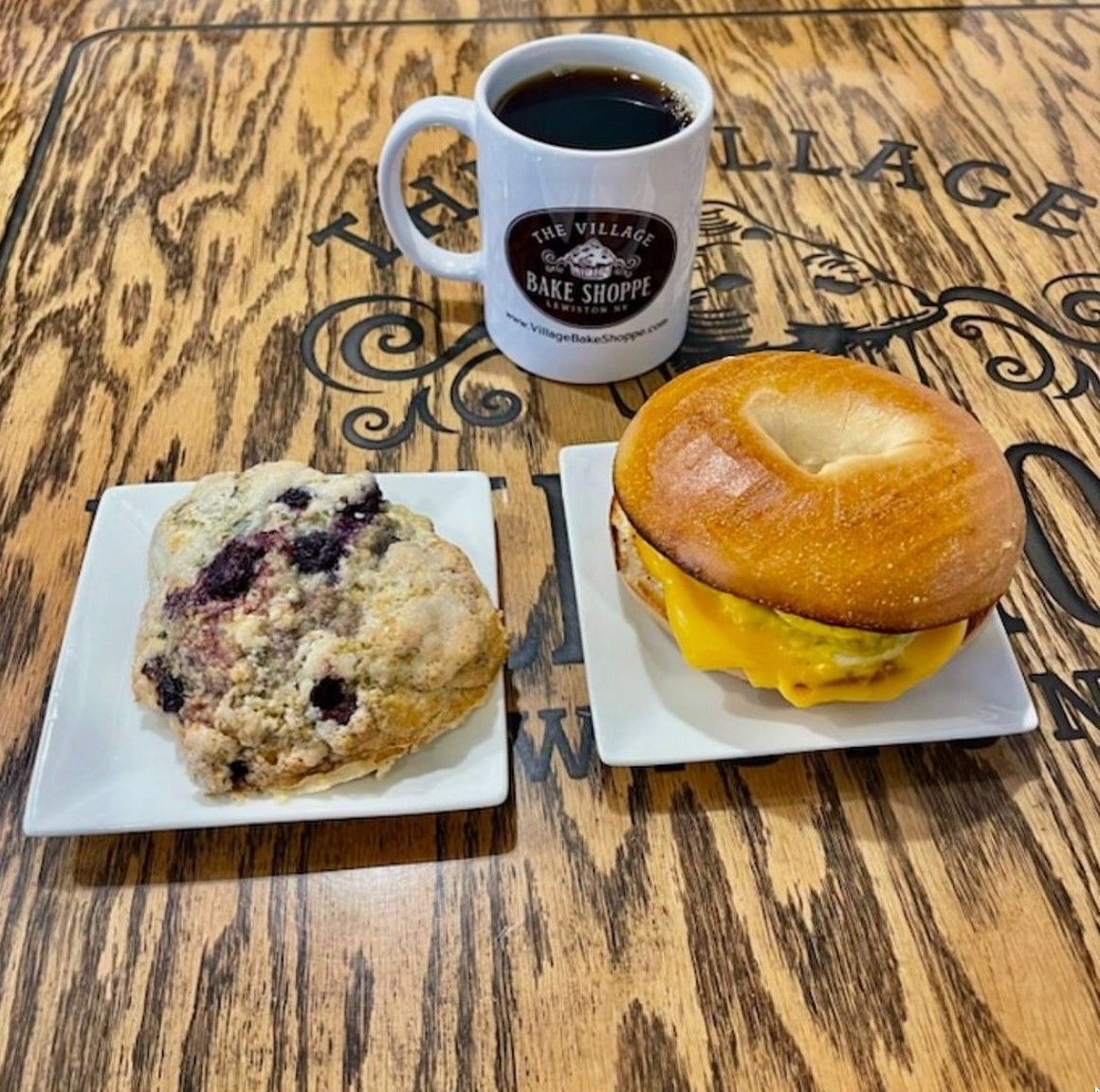 a cup of coffee sits on a wooden table next to a muffin and a bagel