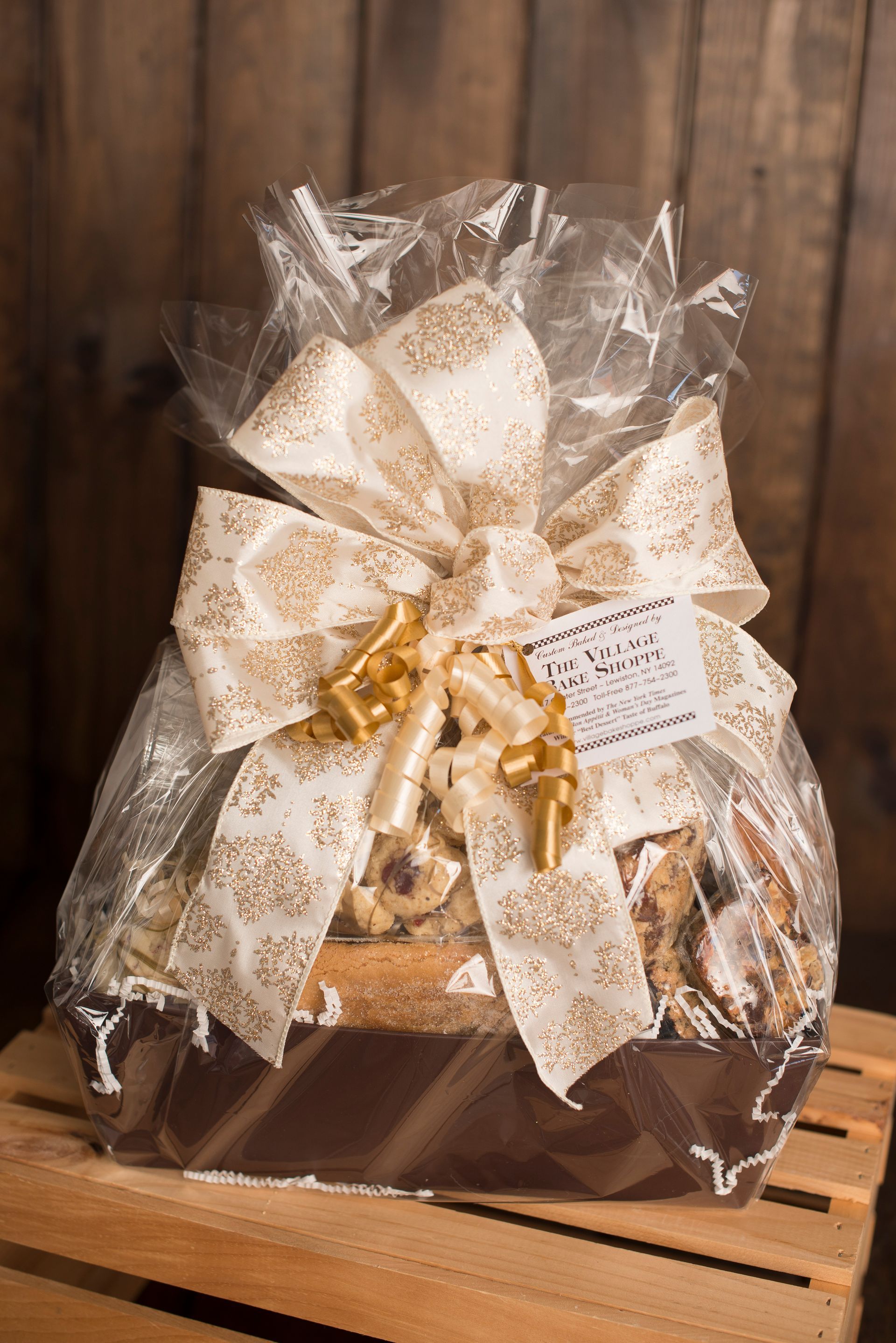 a gift basket wrapped in plastic with a bow is sitting on a wooden crate .