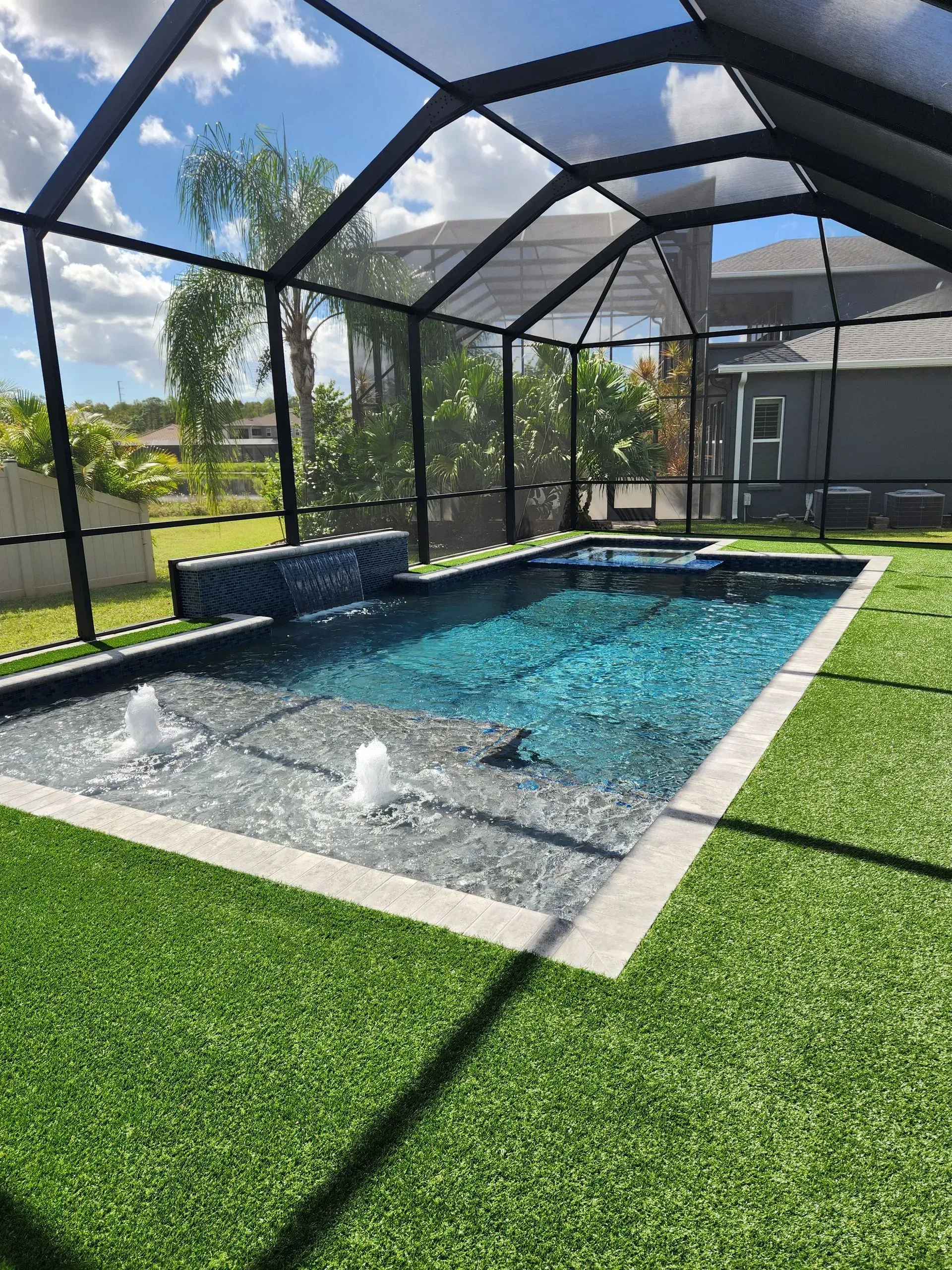A large swimming pool surrounded by grass and a screened in area.