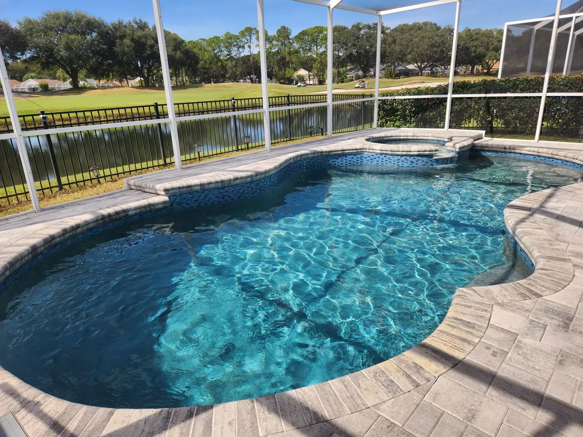 A large swimming pool is surrounded by a screened in area.