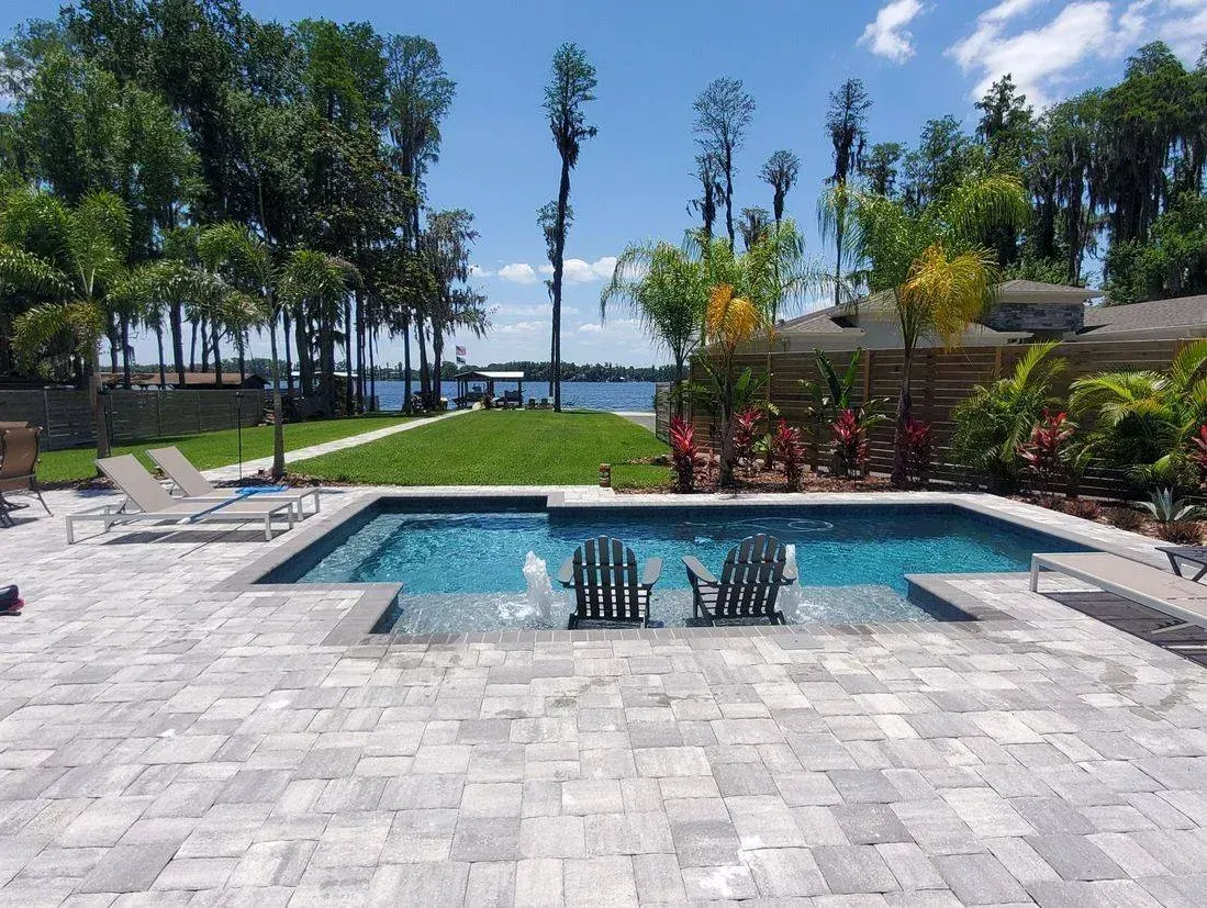 A large swimming pool is surrounded by chairs and a patio