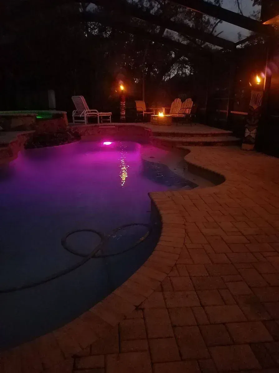 A swimming pool is lit up at night with purple lights.