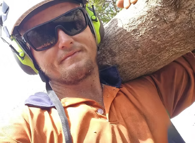A Man Wearing Sunglasses Is Carrying A Tree Branch On His Shoulder — Tropical Tree Solutions in Machans Beach, QLD