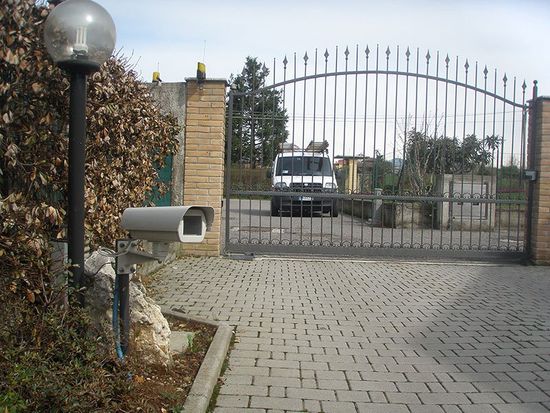 una telecamera di sicurezza installata a basso livello e dietro un cancellone d’entrata con un furgone bianco da lavoro 