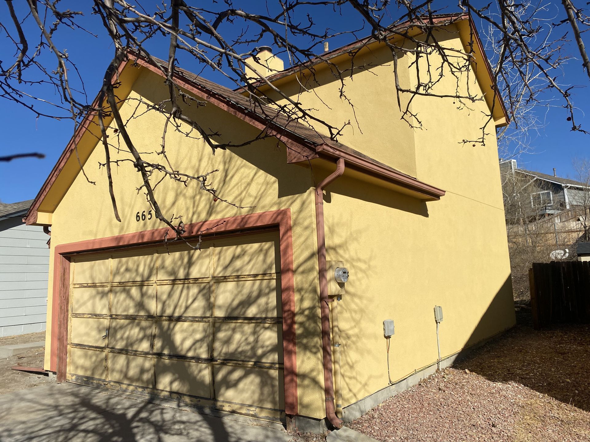 A yellow house with a garage and a tree in the background