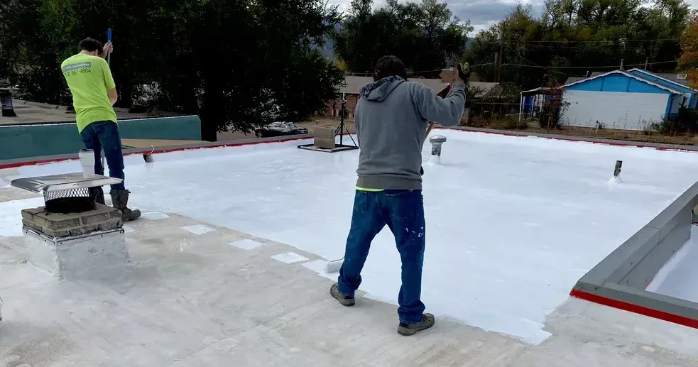Two men are standing on a roof painting it white.