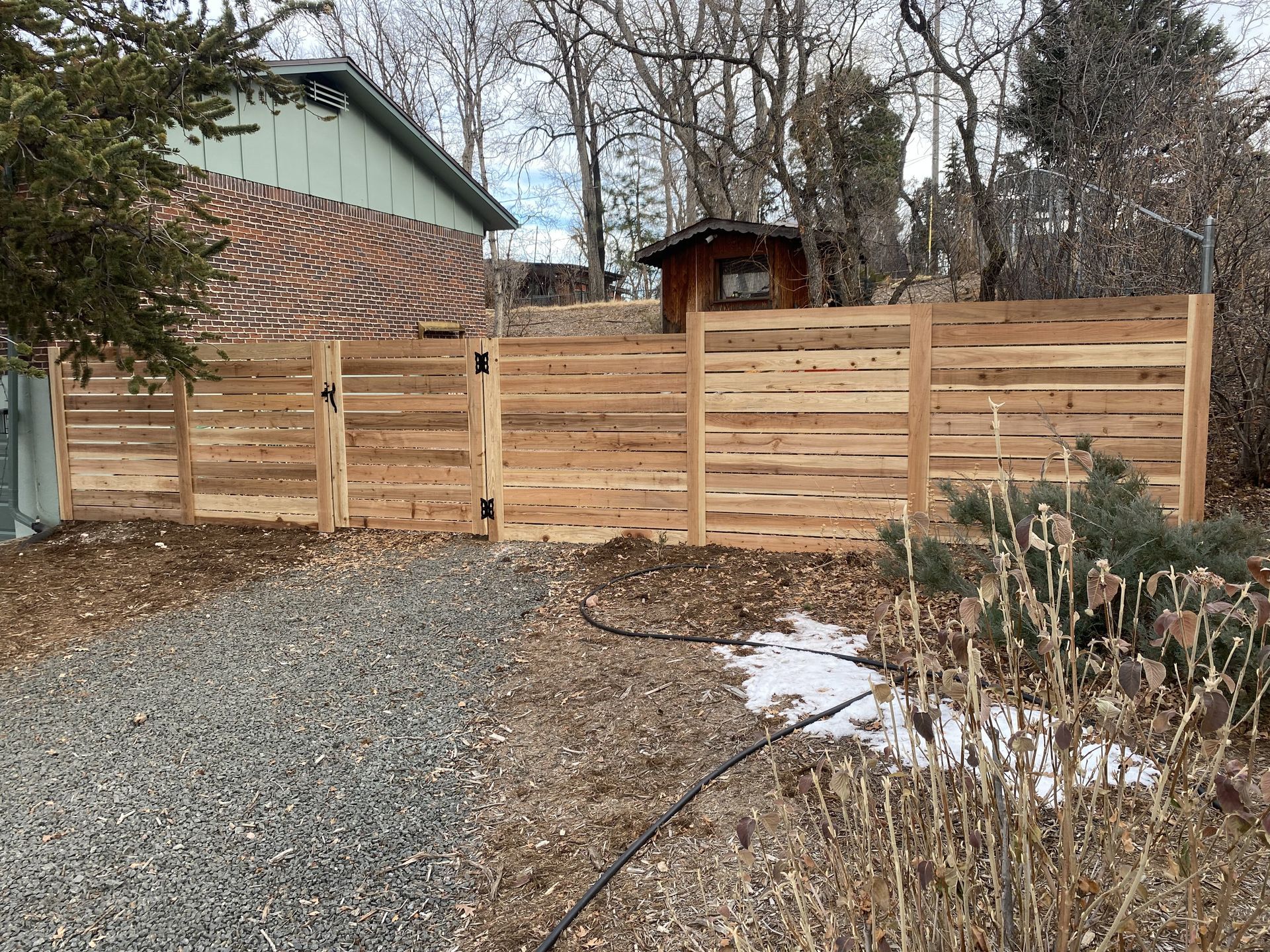A wooden fence is surrounding a gravel driveway in front of a house.