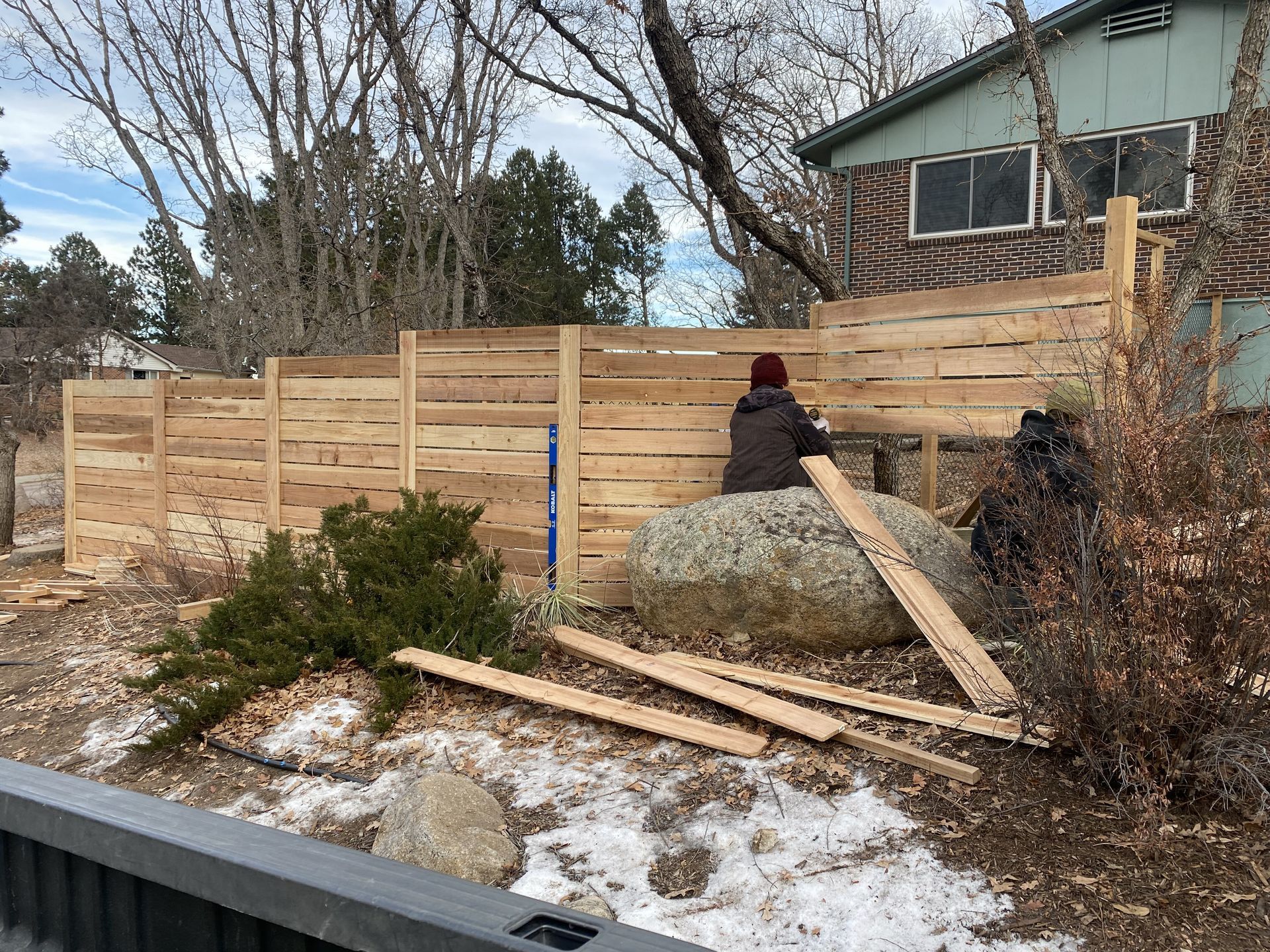 A man is sitting on a rock in front of a wooden fence.