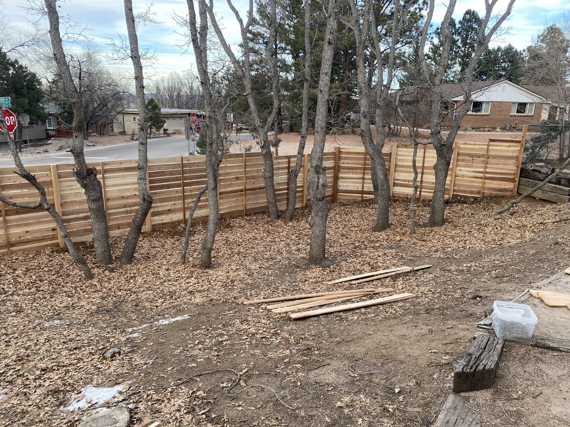 A wooden fence is being built in a backyard surrounded by trees.