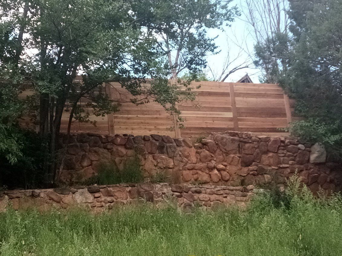 A wooden fence is sitting next to a stone wall in a field.