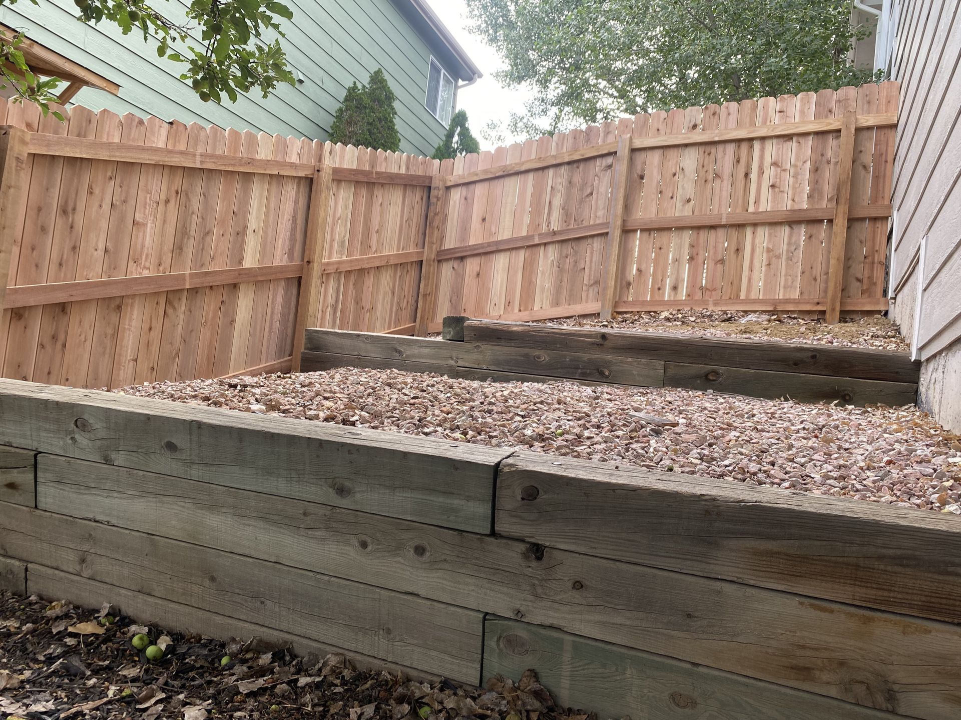A wooden fence is sitting on top of a gravel hill next to a house.