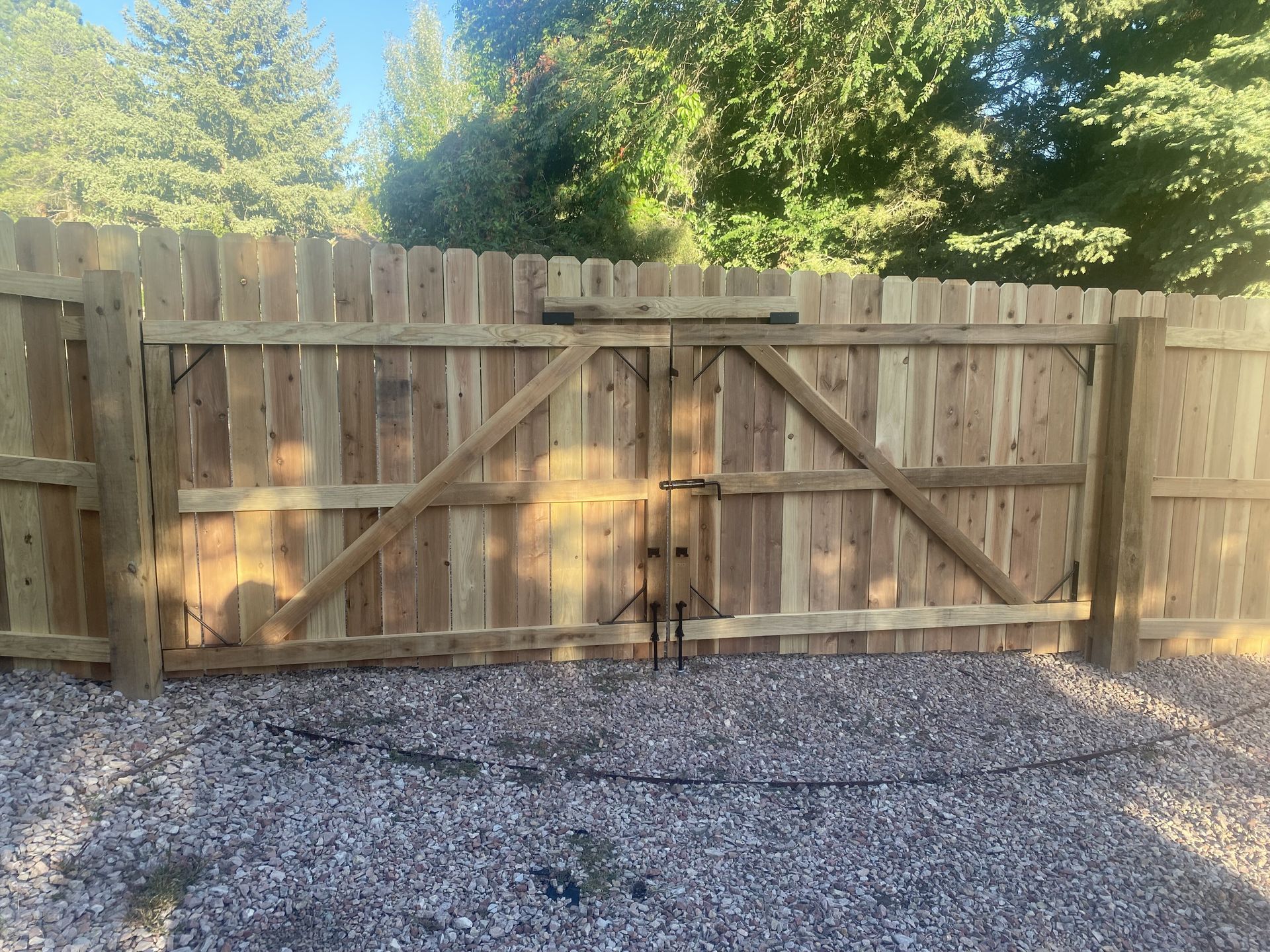 A wooden fence with a gate is surrounded by gravel and trees.