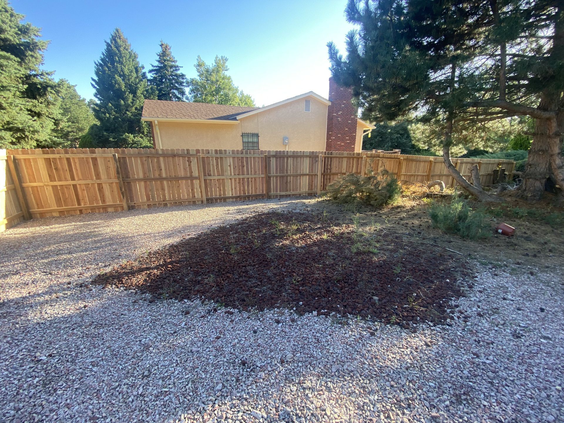 A wooden fence surrounds a gravel driveway in front of a house.