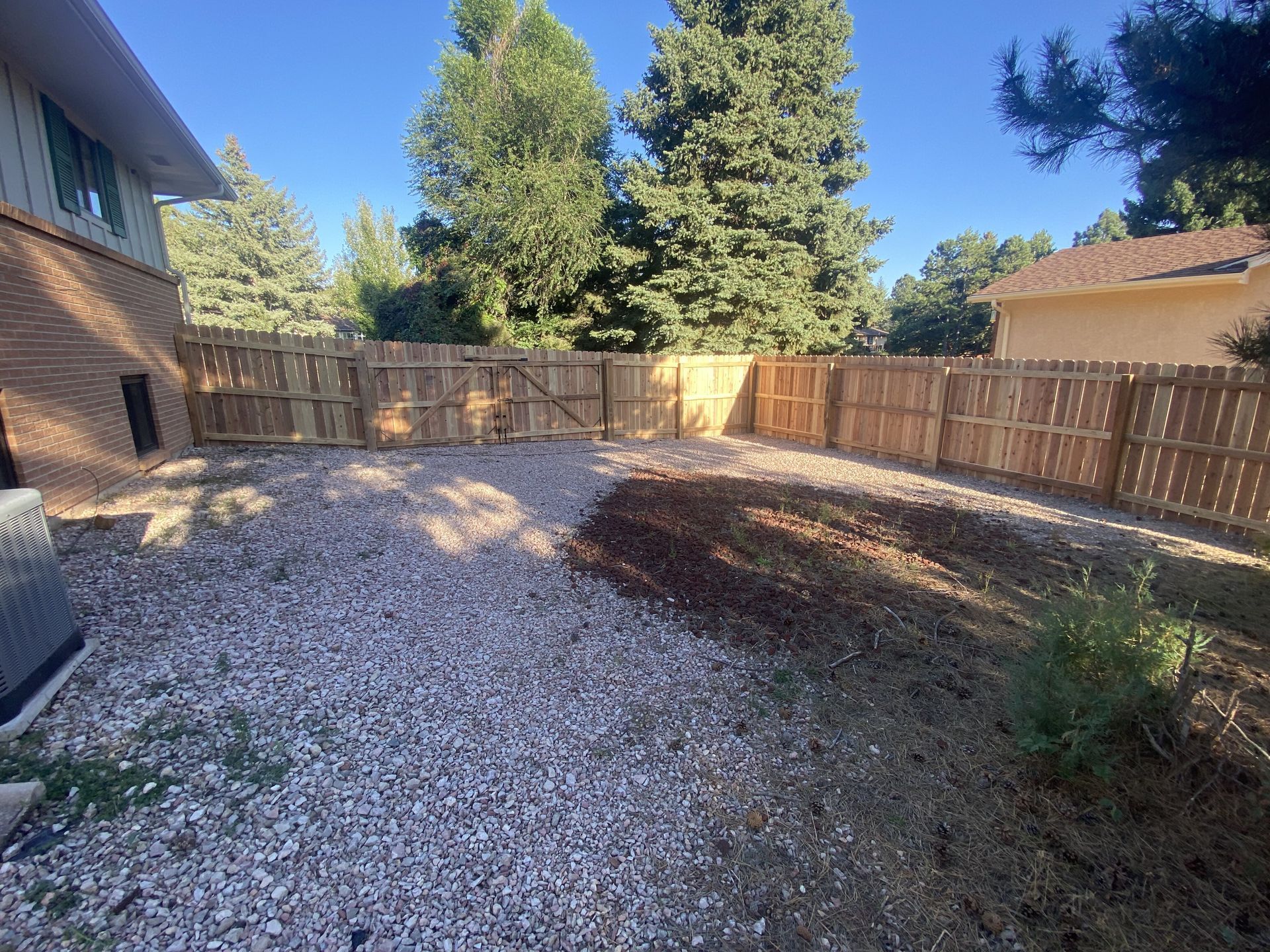 A backyard with a wooden fence and gravel in front of a house.