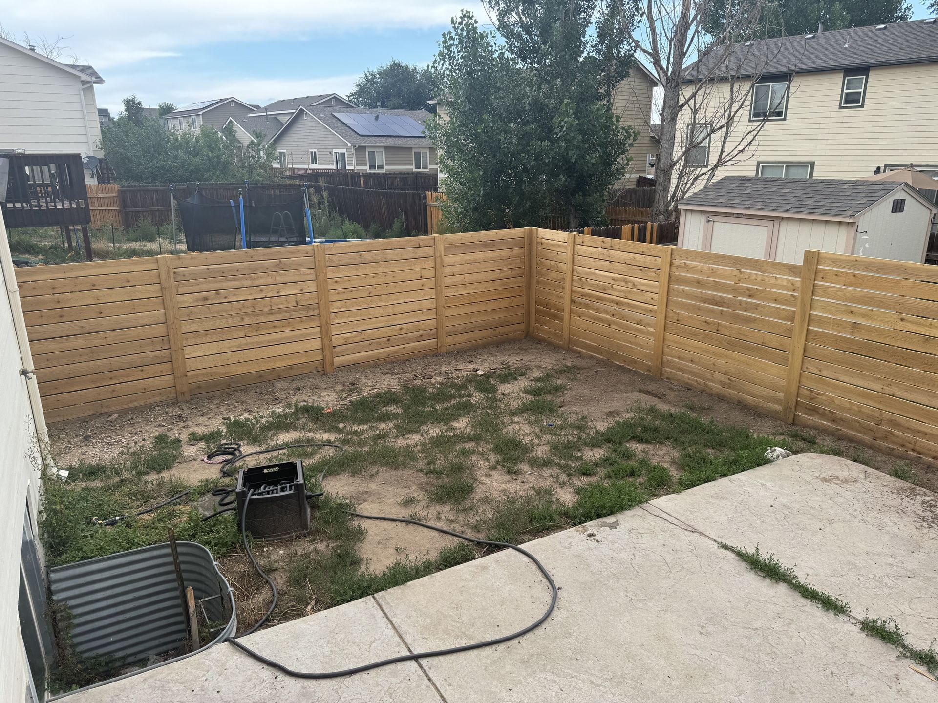 A backyard with a wooden fence and a hose.