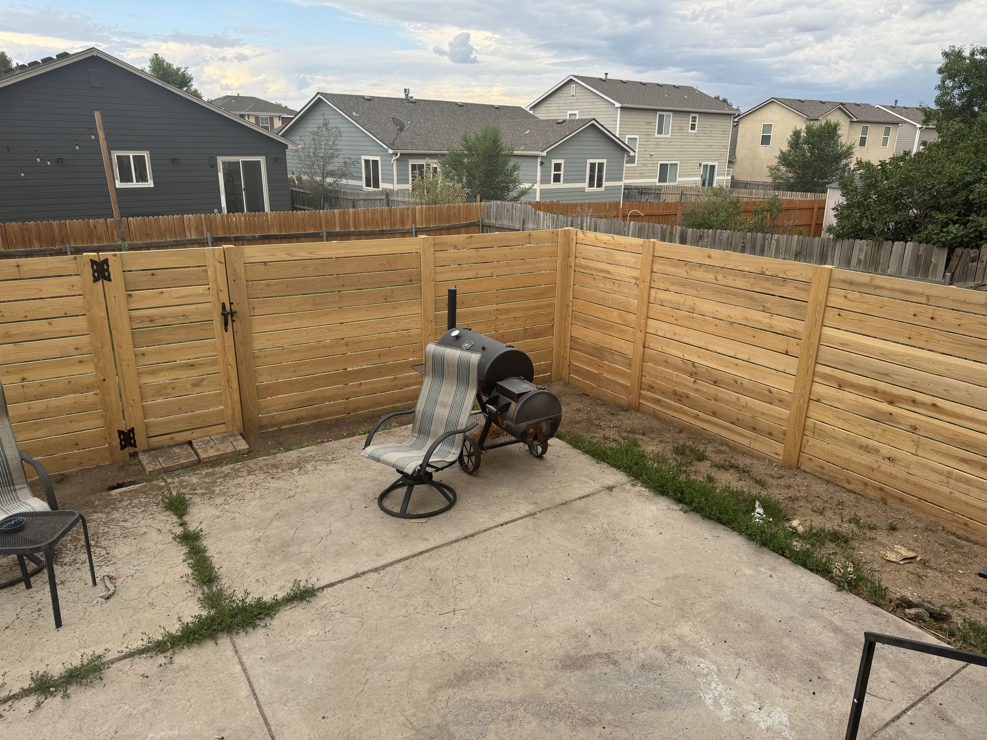 A wooden fence with a chair and a grill in the backyard of a house.