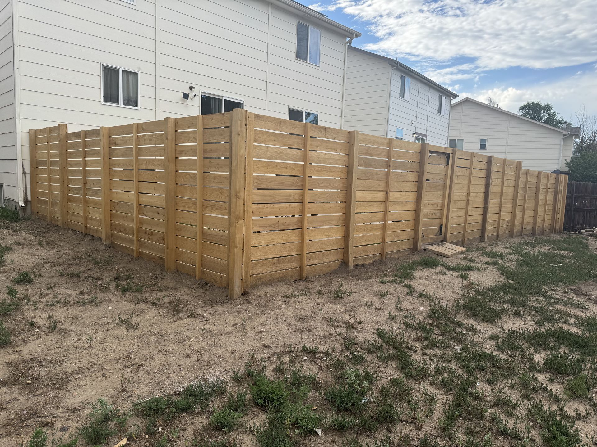 A wooden fence is in the backyard of a house.