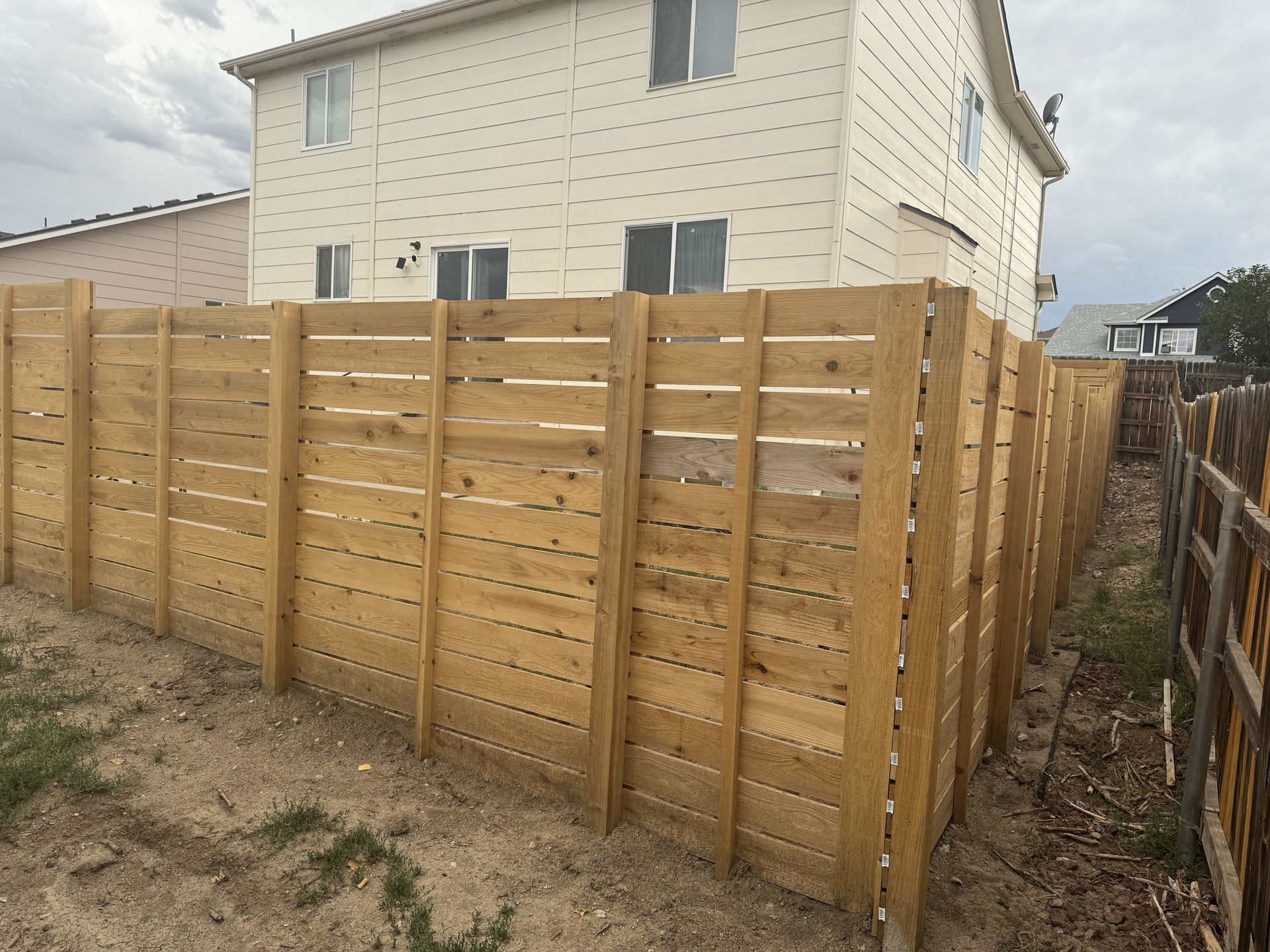A wooden fence is in front of a white house.
