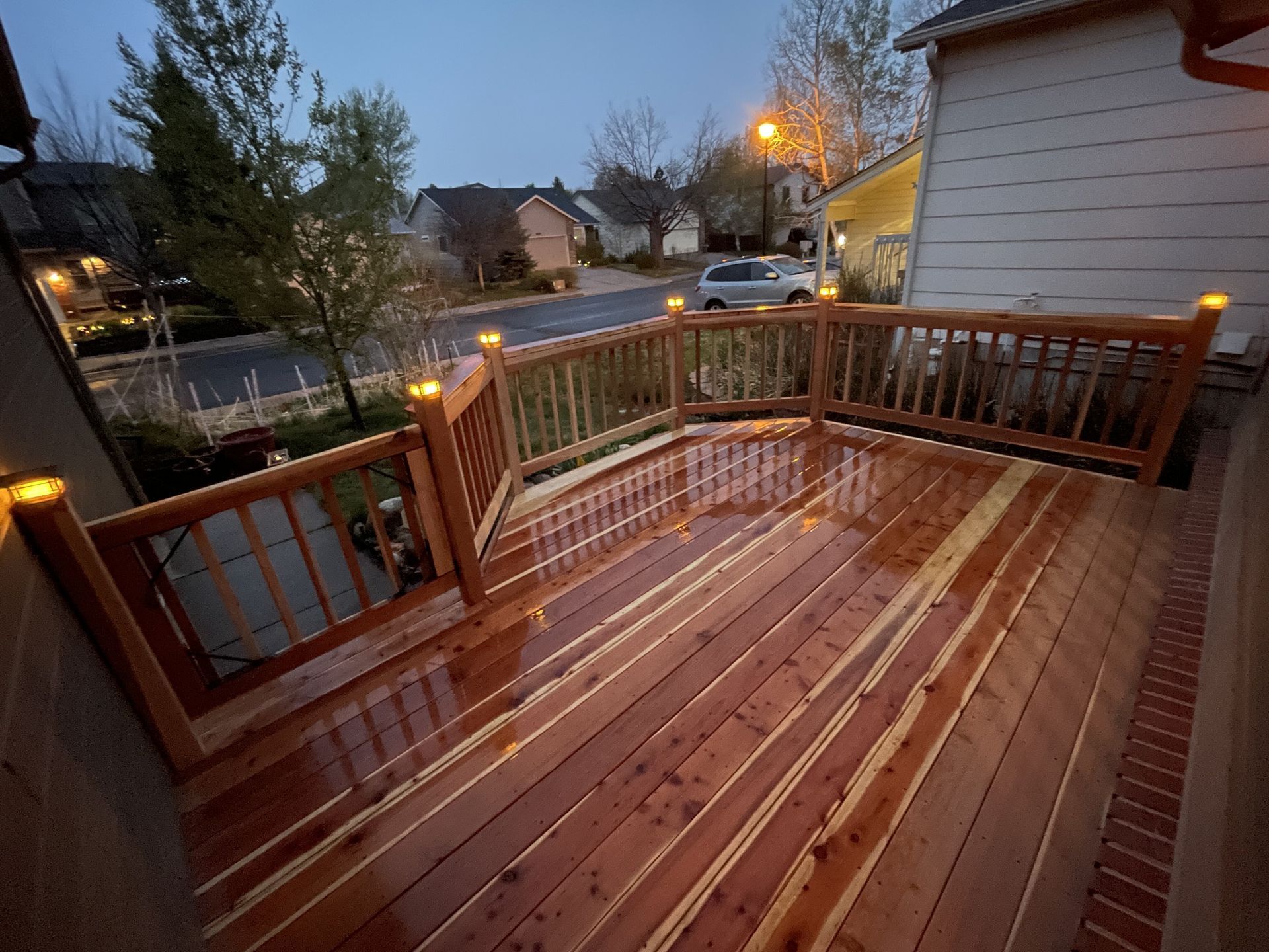 A wooden deck with a railing is lit up at night.
