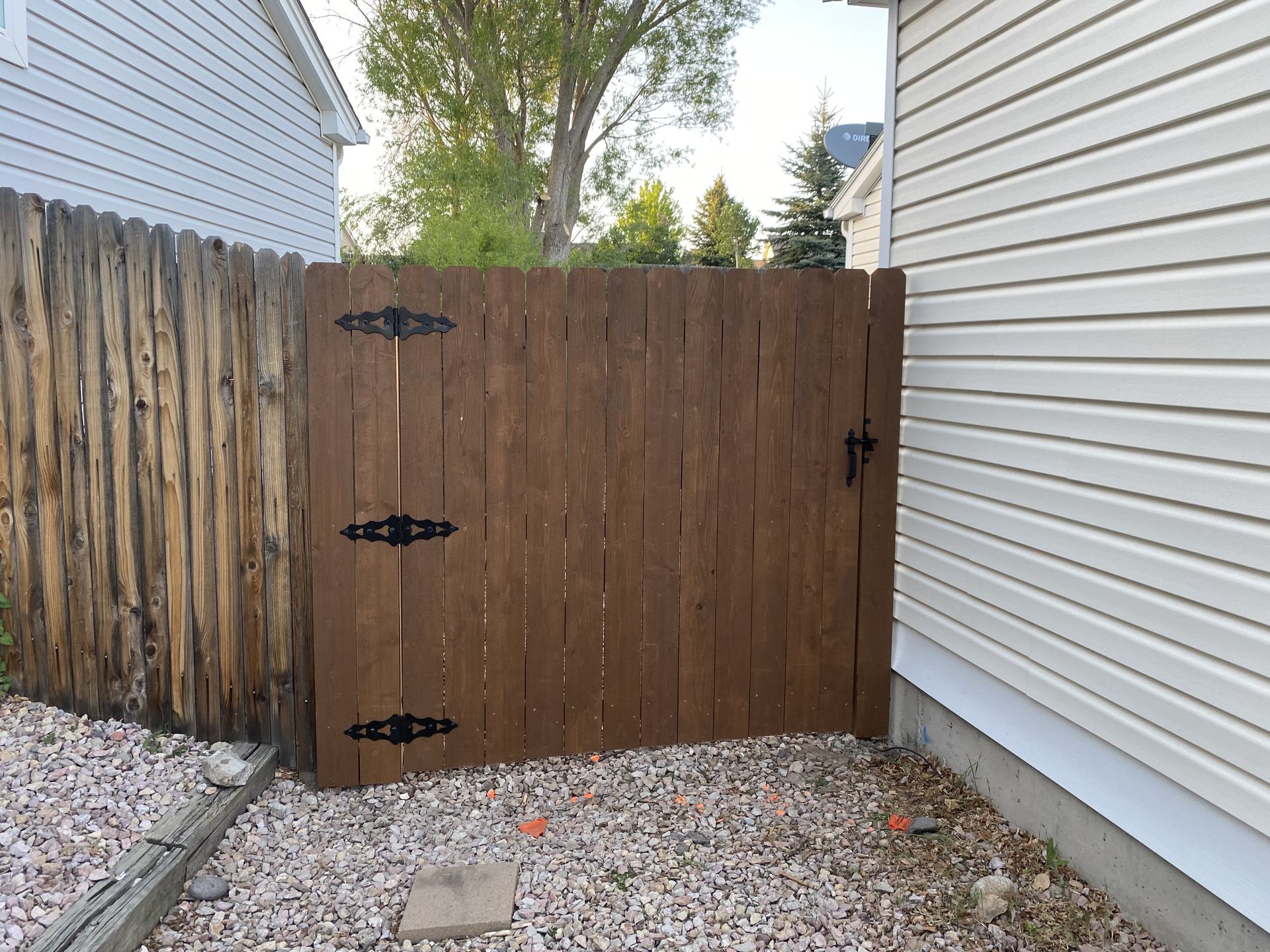 A wooden fence is surrounded by gravel next to a house.