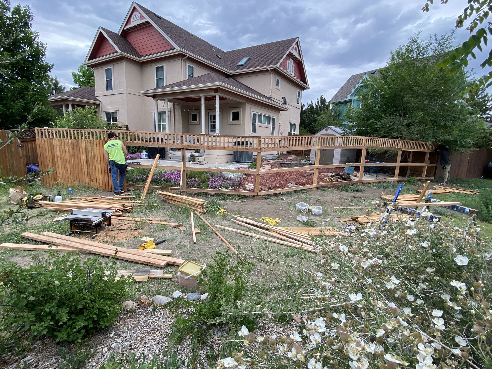 A man is standing in front of a house with a wooden fence in the backyard.