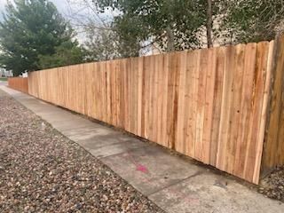 A wooden fence along a sidewalk next to a gravel road.